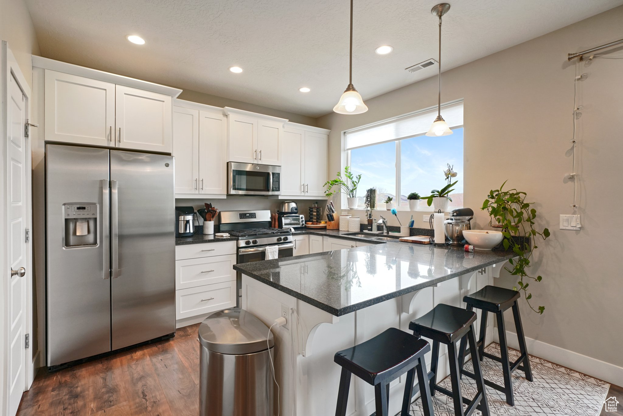 Kitchen with stainless steel appliances, dark wood-type flooring, a peninsula, and white cabinetry