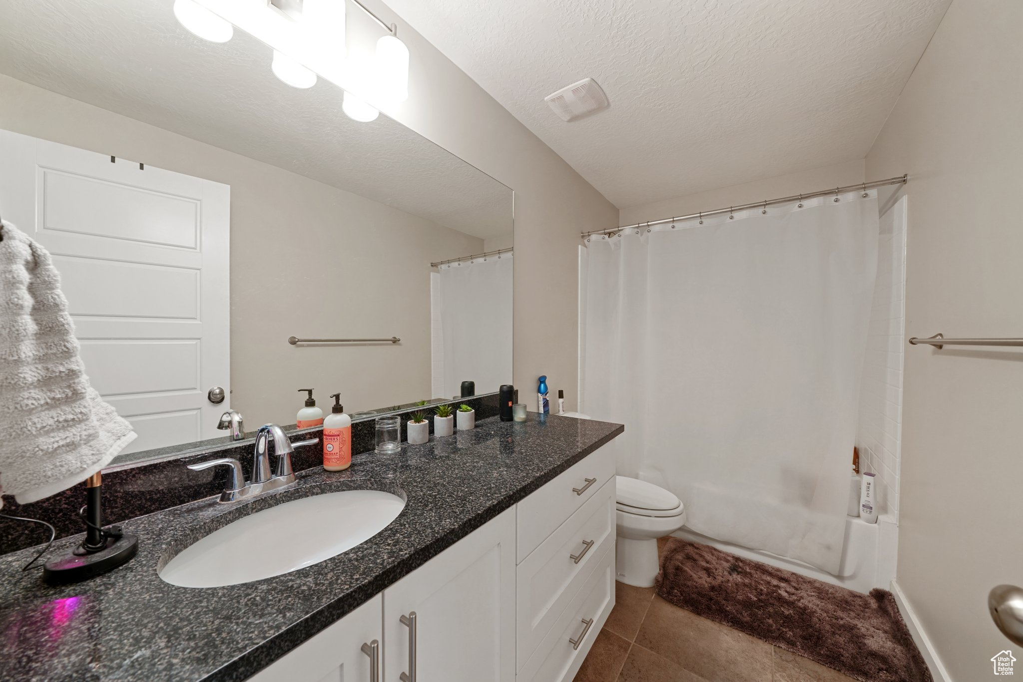 Full bath with vanity, shower / bath combo with shower curtain, a textured ceiling, tile patterned floors, and toilet