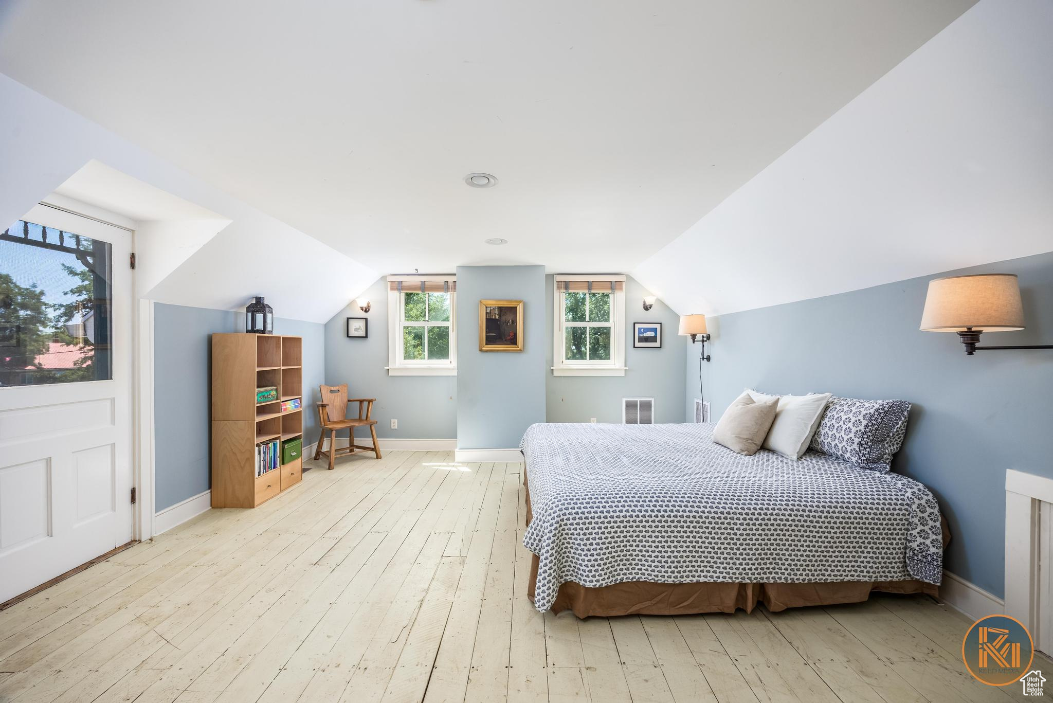 Bedroom featuring light wood finished floors, visible vents, baseboards, and vaulted ceiling