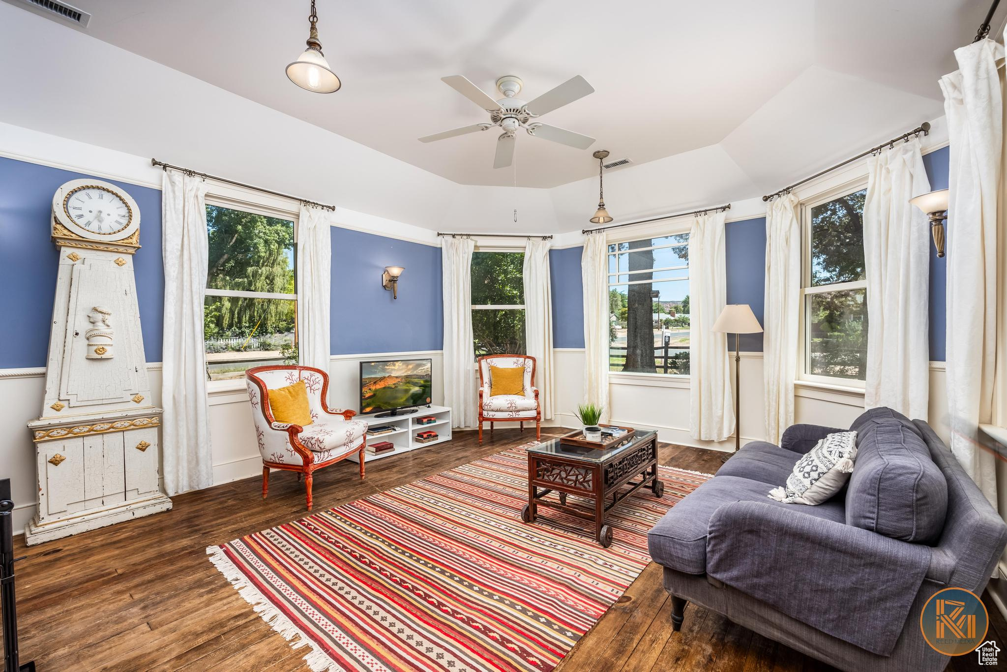 Living area featuring a tray ceiling, a wainscoted wall, visible vents, ceiling fan, and wood finished floors