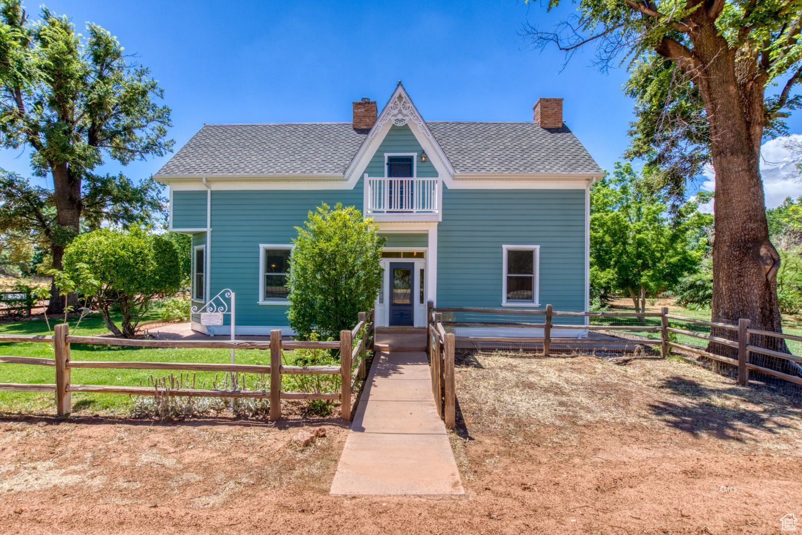 Victorian home with a chimney, roof with shingles, fence, and a balcony