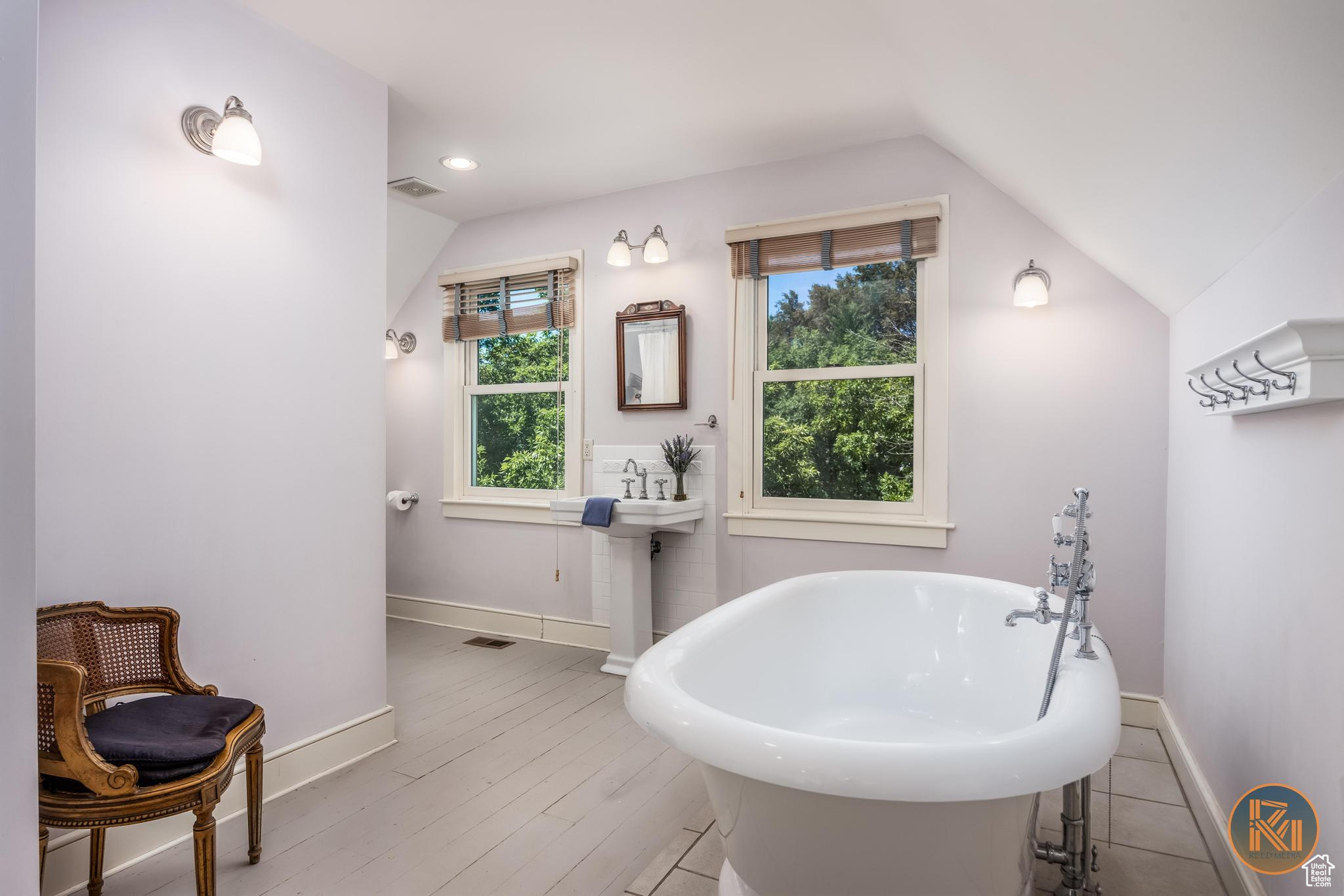 Full bath featuring a freestanding tub, baseboards, vaulted ceiling, and wood finished floors