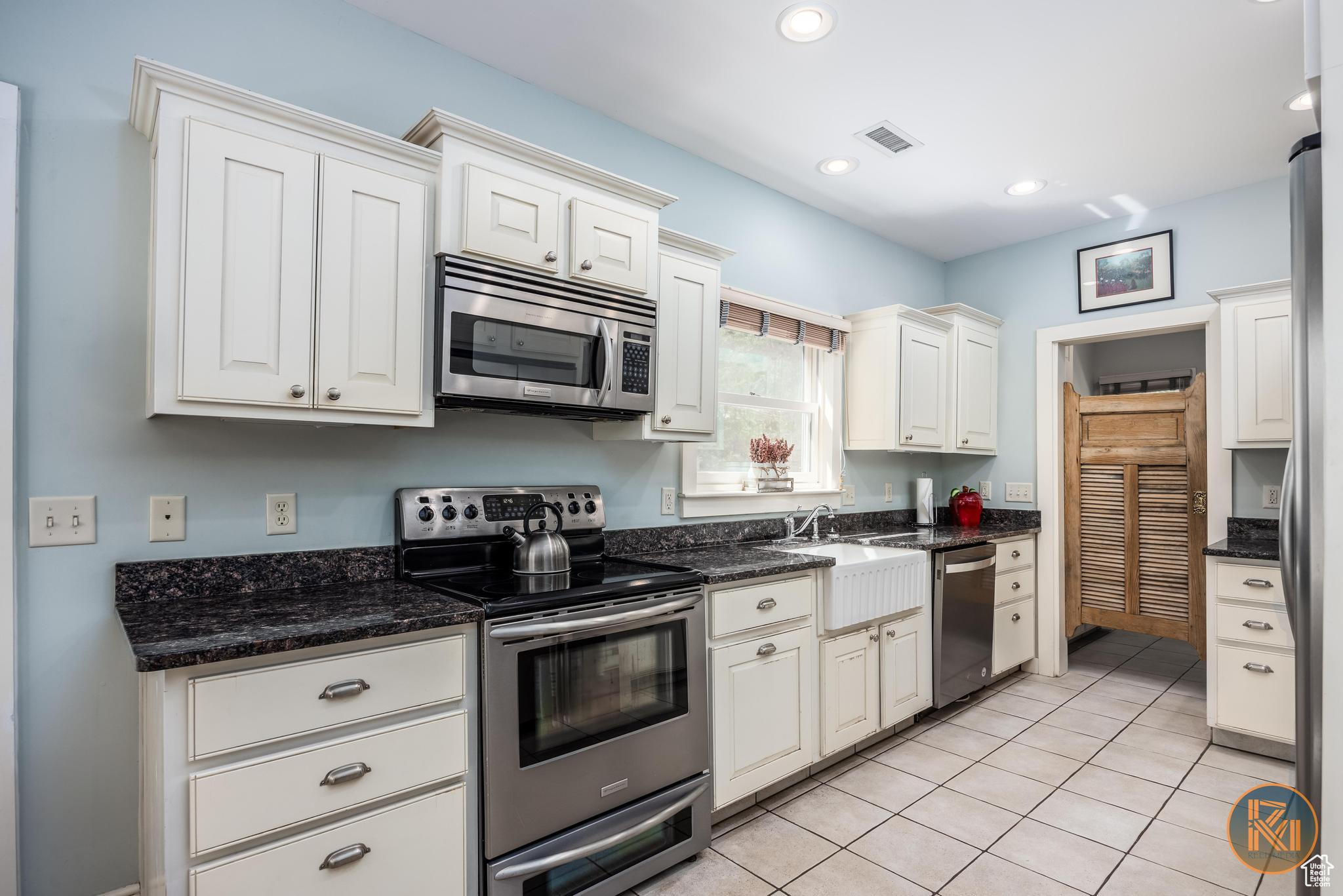 Kitchen with stainless steel appliances, recessed lighting, visible vents, light tile patterned flooring, and a sink