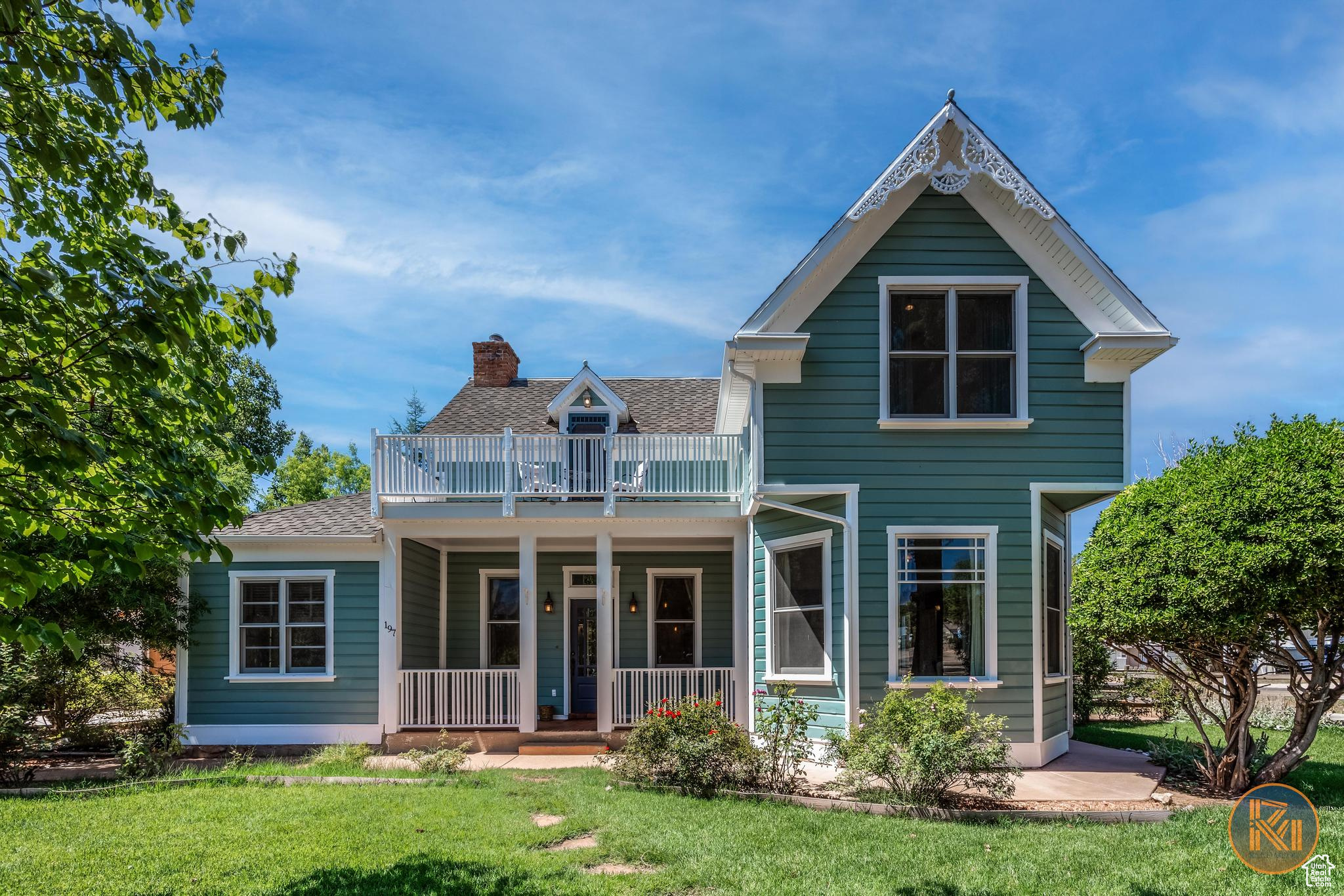 View of front of property with a chimney, a porch, a shingled roof, a front yard, and a balcony