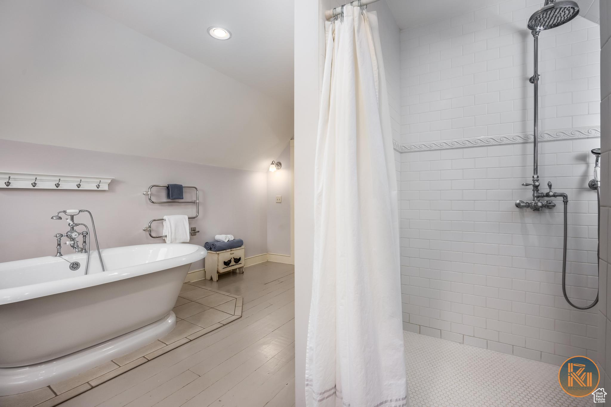 Bathroom with lofted ceiling, wood finished floors, baseboards, a soaking tub, and a tile shower