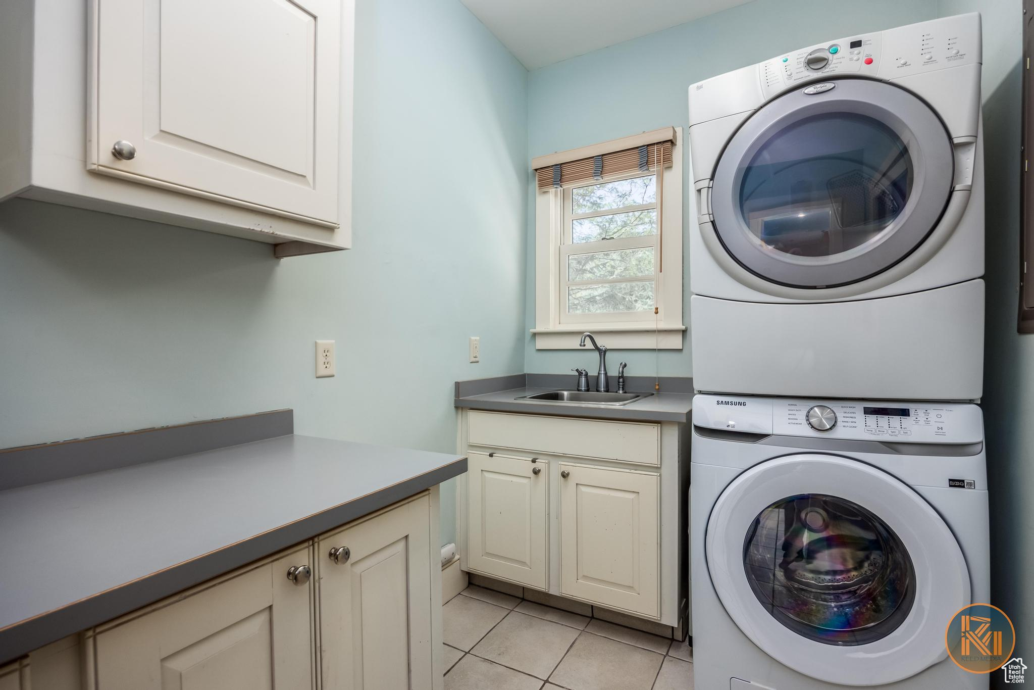 Clothes washing area featuring stacked washer / dryer, cabinet space, light tile patterned floors, and a sink