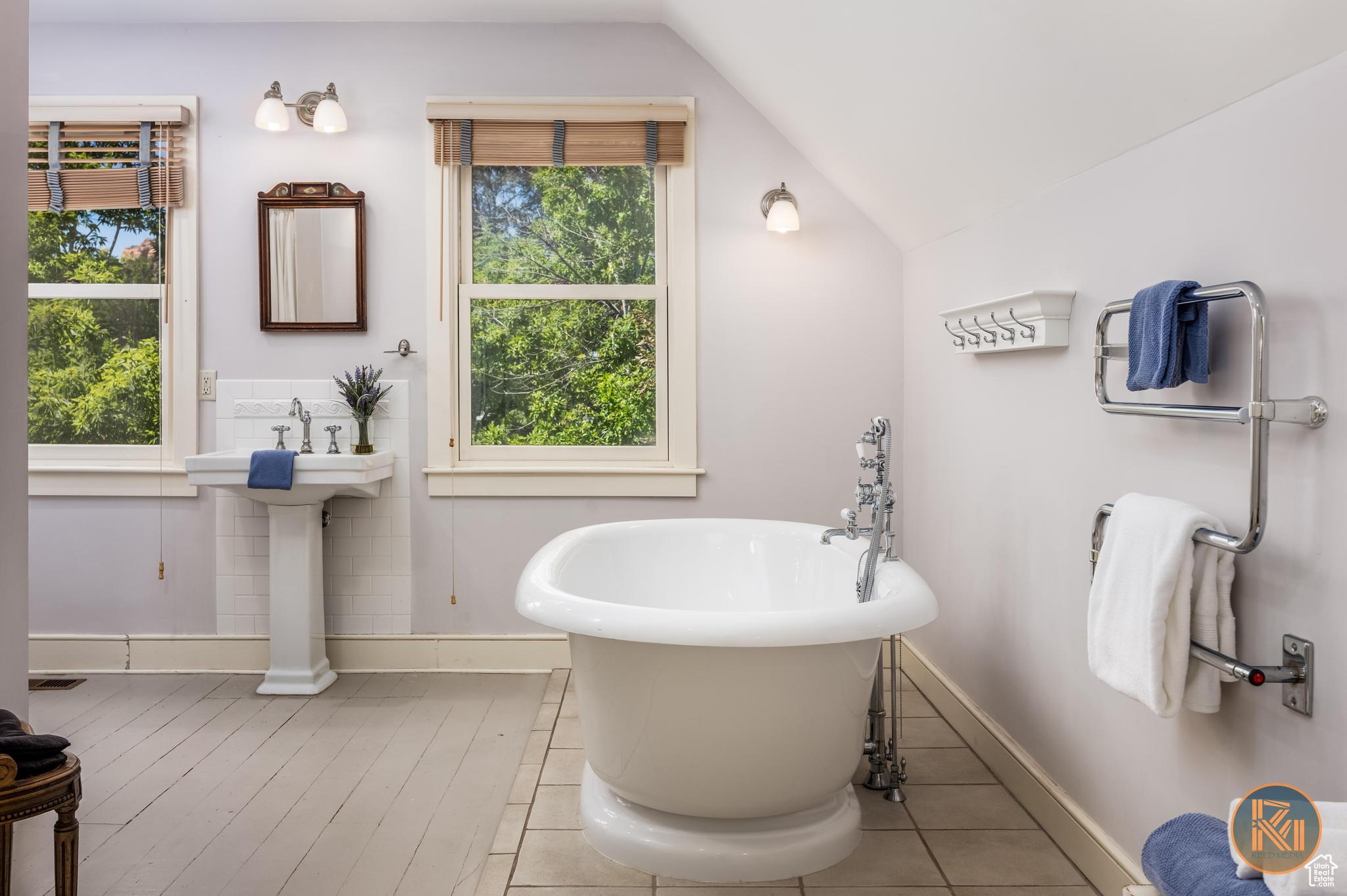Bathroom featuring a healthy amount of sunlight, a freestanding tub, baseboards, and vaulted ceiling