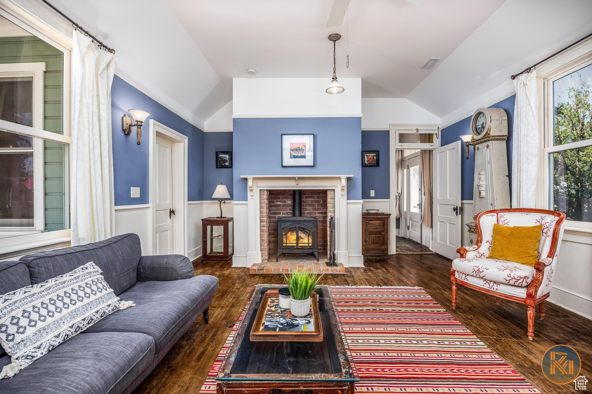 Living area featuring lofted ceiling, a wood stove, a wainscoted wall, and wood finished floors