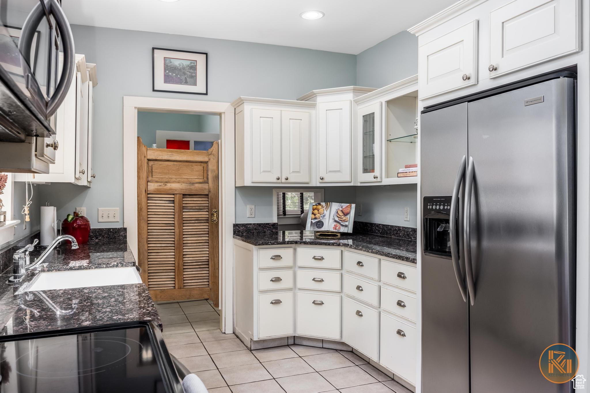 Kitchen featuring light tile patterned flooring, a sink, white cabinetry, black electric range, and stainless steel fridge with ice dispenser