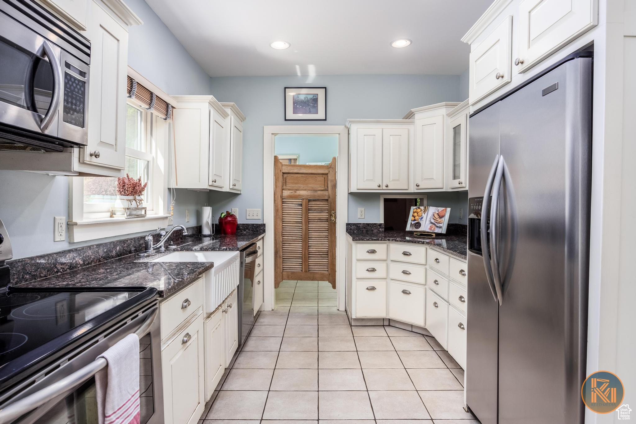 Kitchen with light tile patterned floors, appliances with stainless steel finishes, and white cabinetry