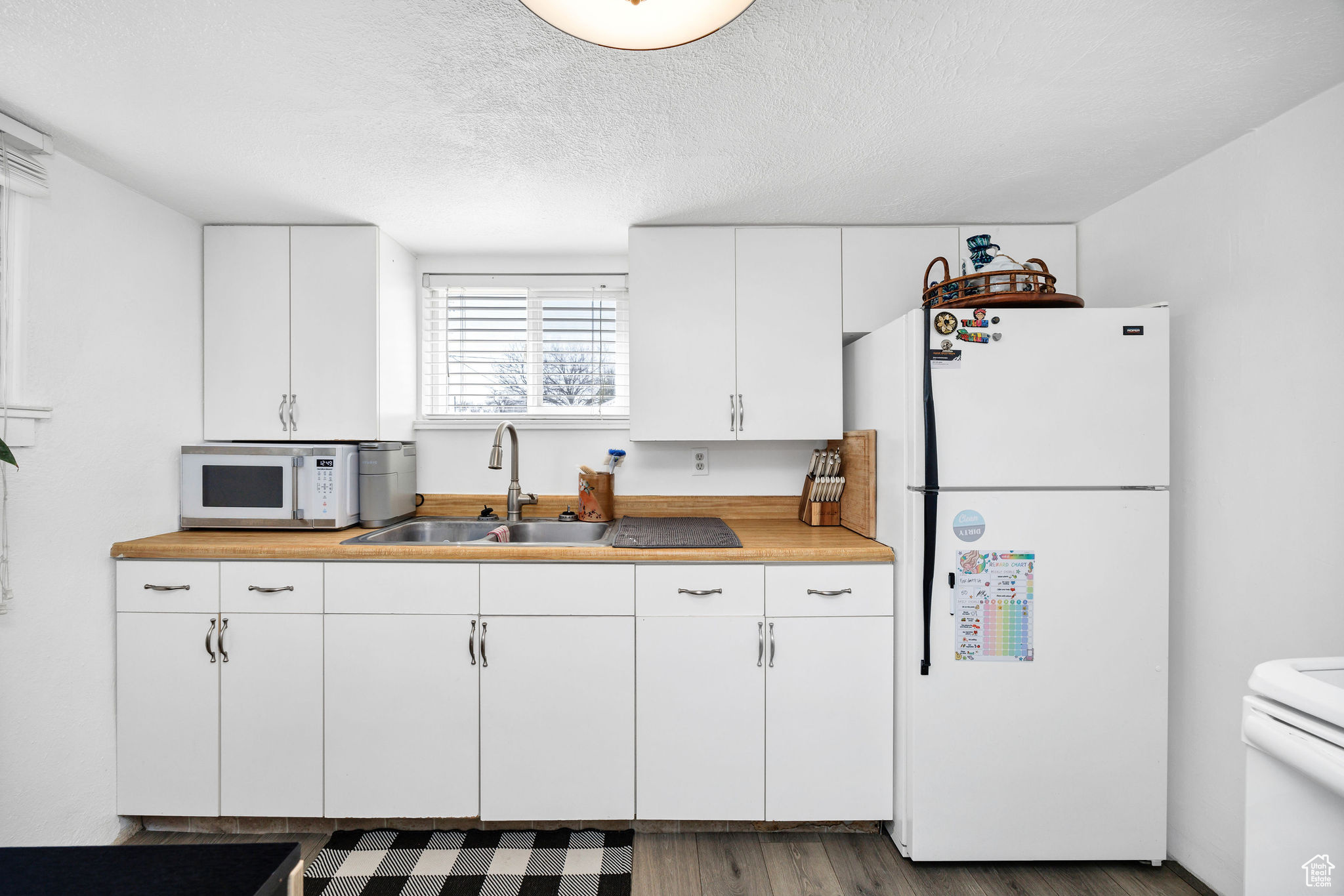 Kitchen featuring a sink, wood finished floors, white appliances, white cabinets, and light countertops