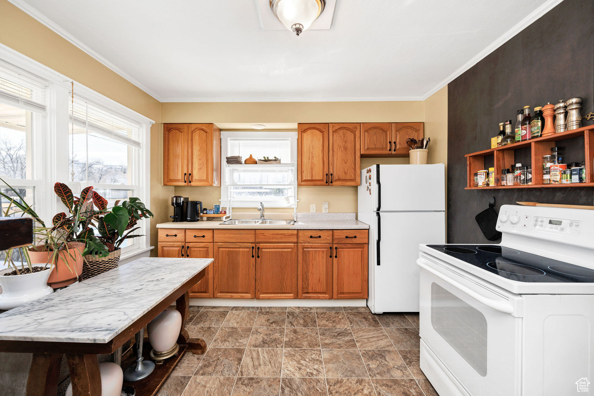 Kitchen featuring white appliances, brown cabinetry, ornamental molding, a sink, and light countertops