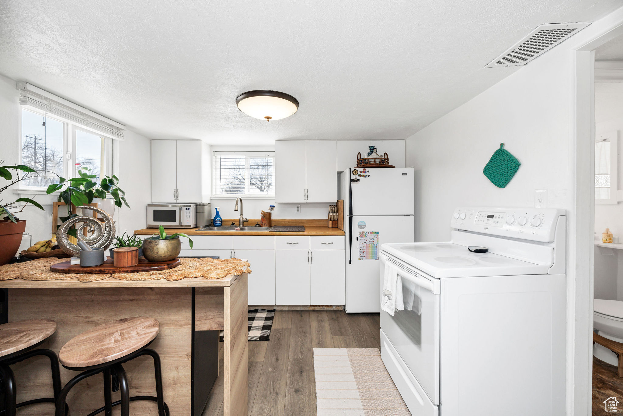 Kitchen with a sink, visible vents, white appliances, and a healthy amount of sunlight