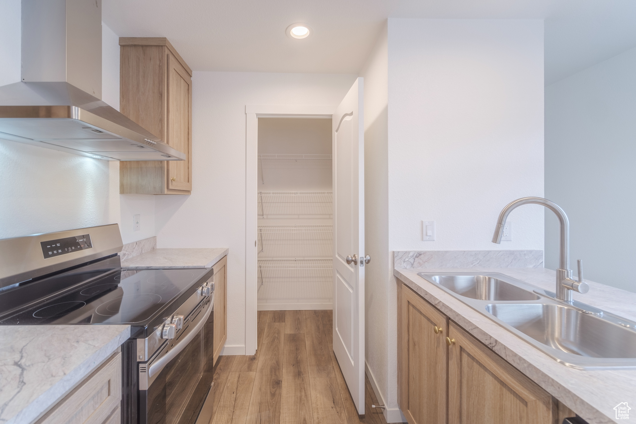 Kitchen with electric range, light brown cabinets, a sink, light wood-style floors, and wall chimney exhaust hood