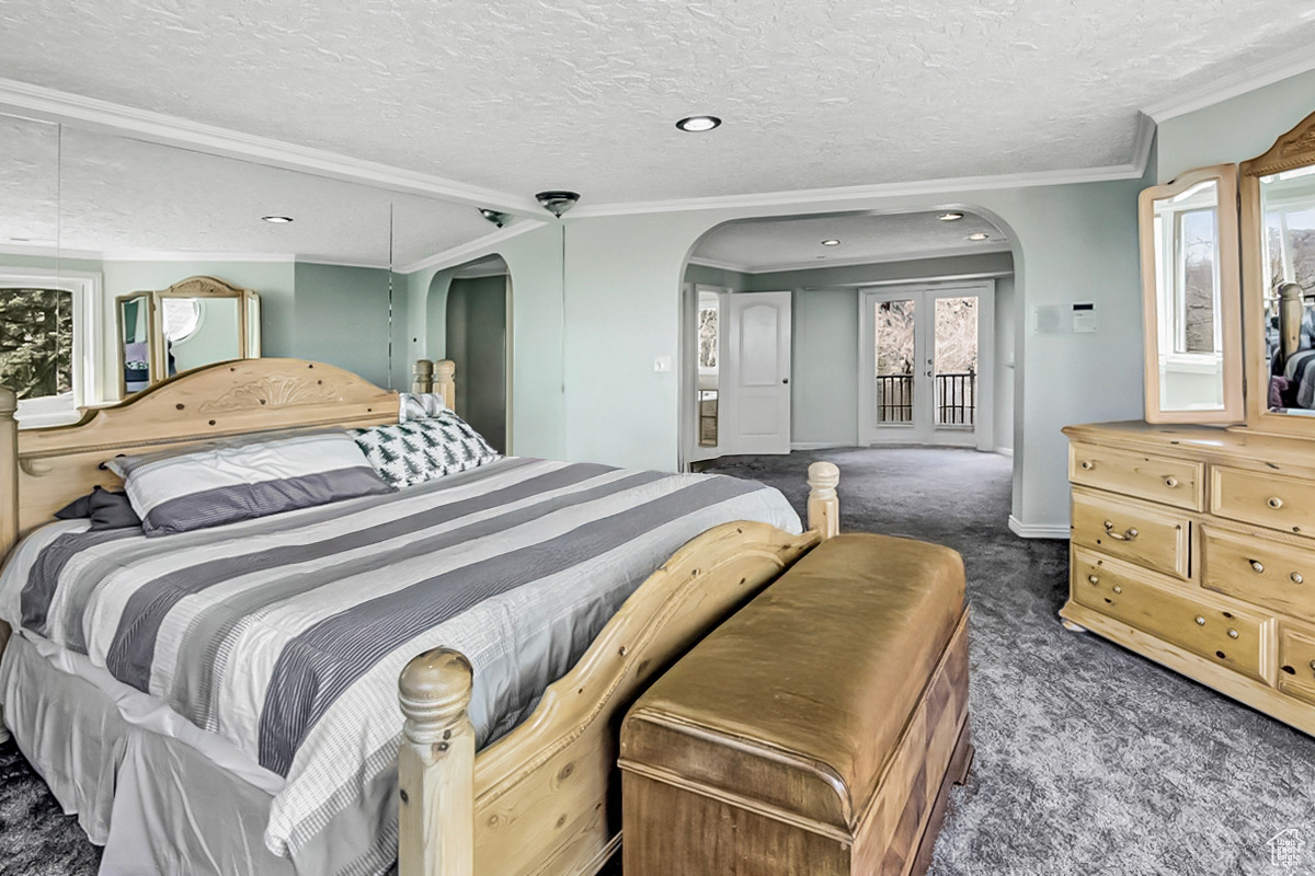 Bedroom featuring arched walkways, a textured ceiling, ornamental molding, and carpet flooring