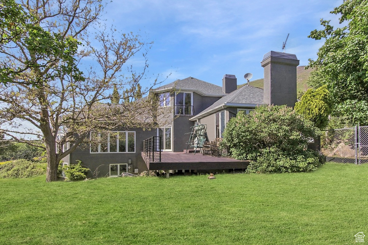Back of house featuring a chimney, a lawn, a wooden deck, and fence