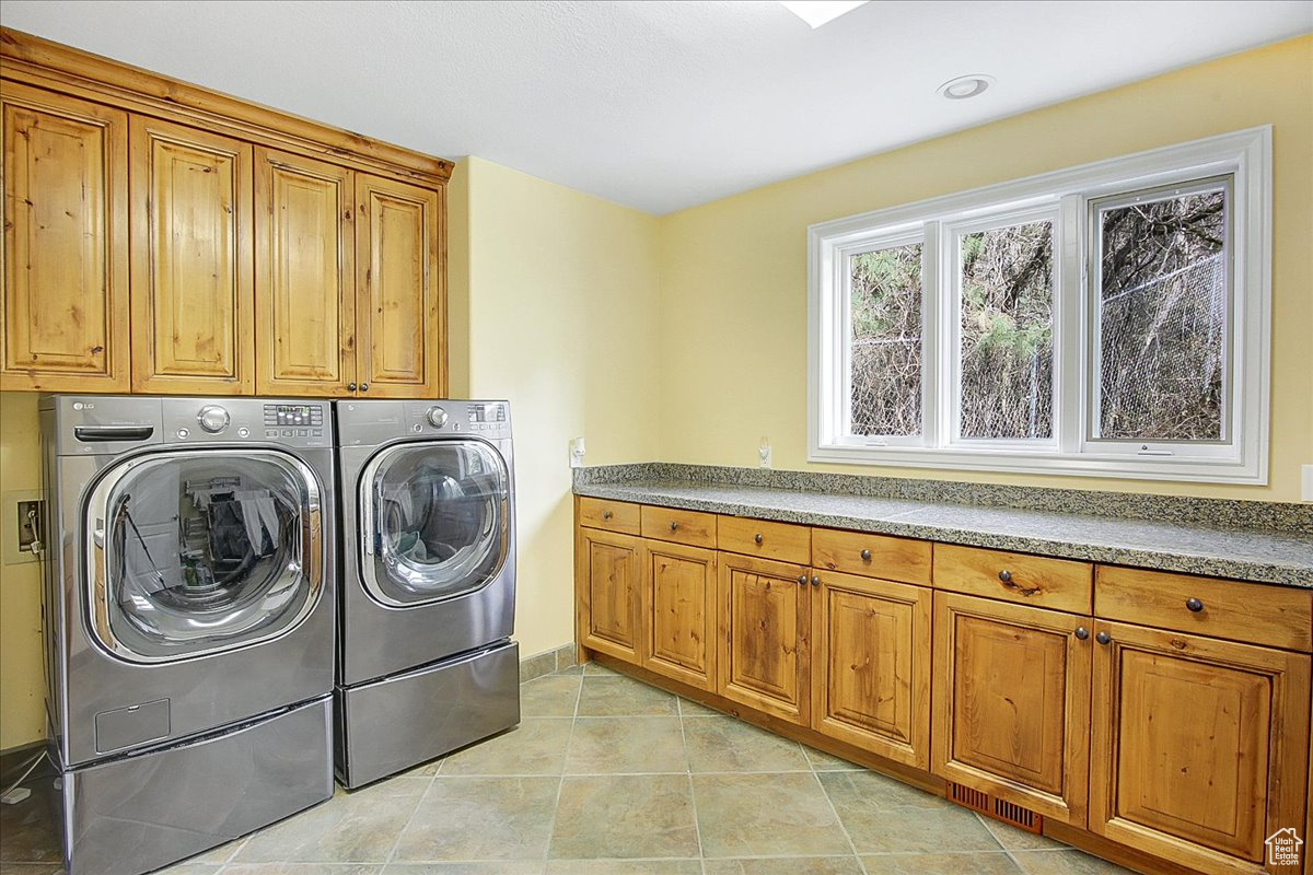Laundry area with light tile patterned floors, washing machine and dryer, and cabinet space
