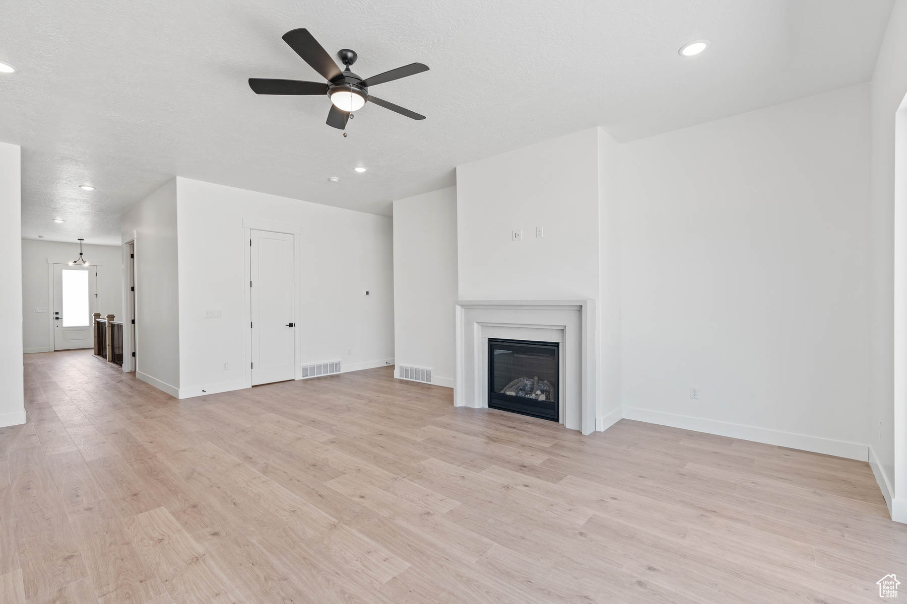 Unfurnished living room with light wood-type flooring, visible vents, a glass covered fireplace, and a ceiling fan