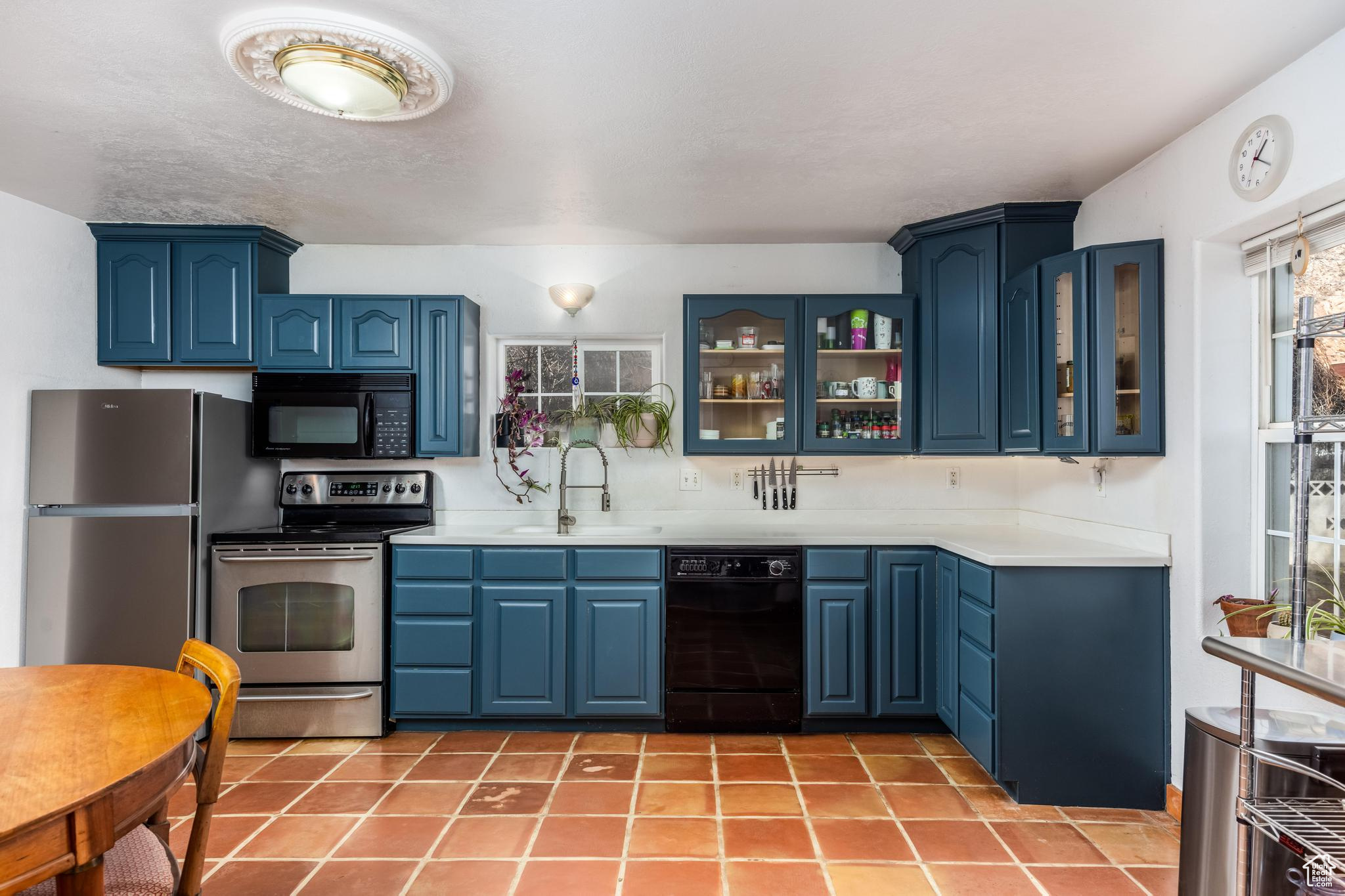 Kitchen with blue cabinetry, black appliances, light countertops, and a sink