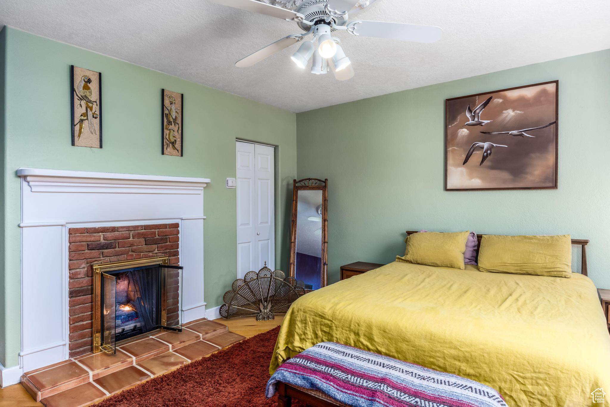 Bedroom with wood finished floors, a ceiling fan, baseboards, a closet, and a brick fireplace