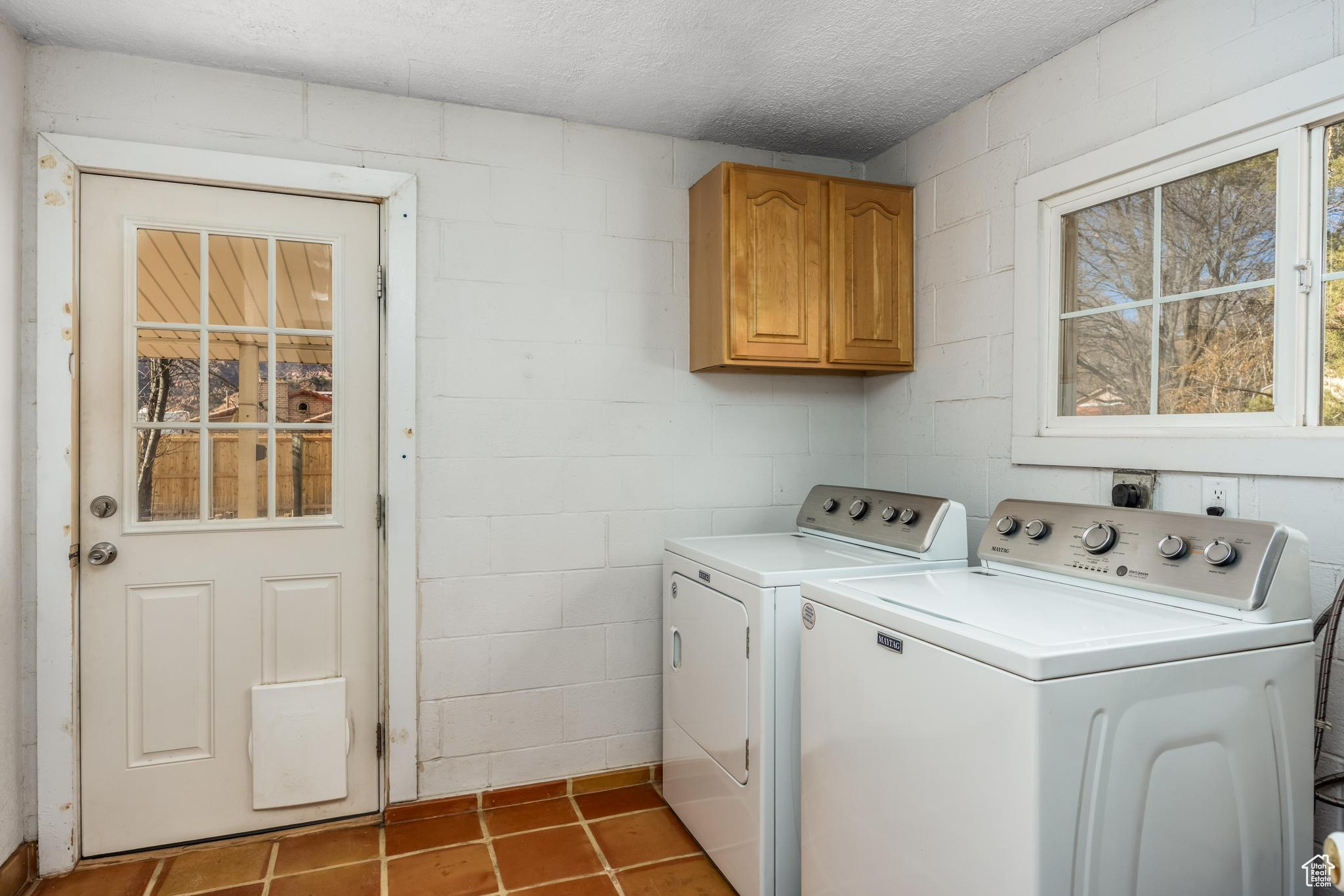 Clothes washing area featuring washer and dryer, a textured ceiling, cabinet space, light tile patterned flooring, and concrete block wall