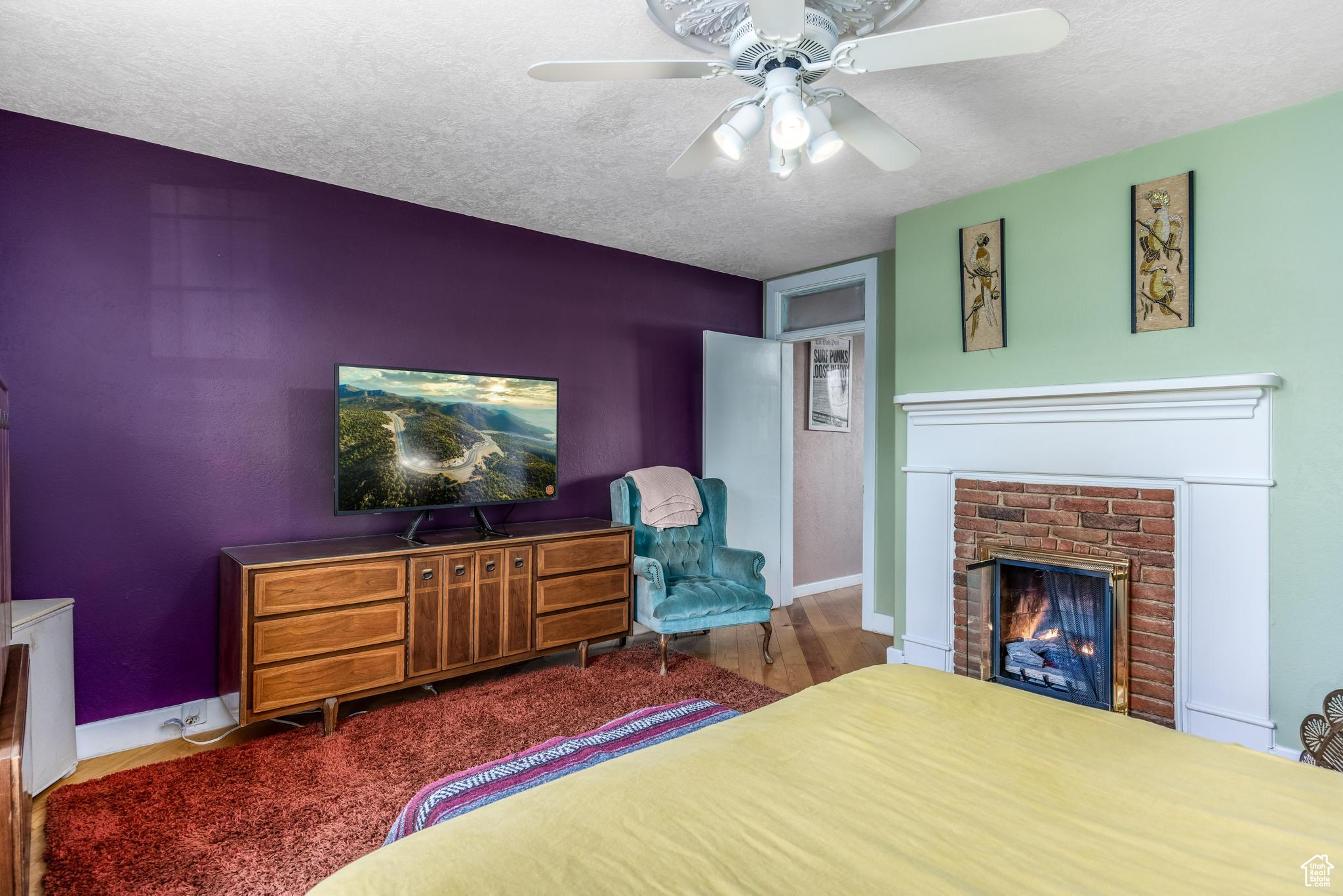 Bedroom with a textured ceiling, wood finished floors, a fireplace, baseboards, and ceiling fan