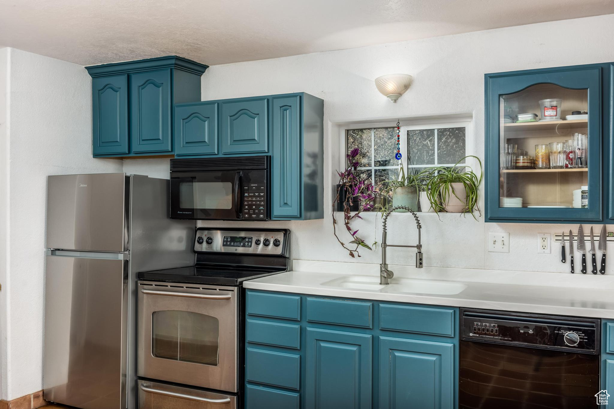 Kitchen featuring black appliances, blue cabinets, light countertops, and a sink