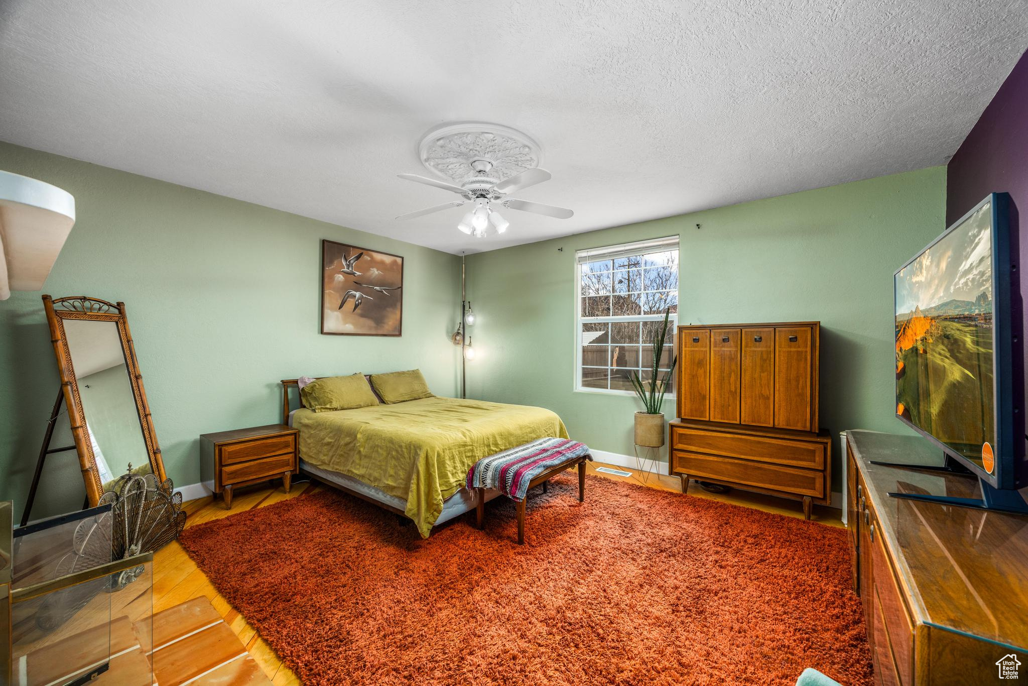 Bedroom featuring ceiling fan, wood finished floors, baseboards, and a textured ceiling