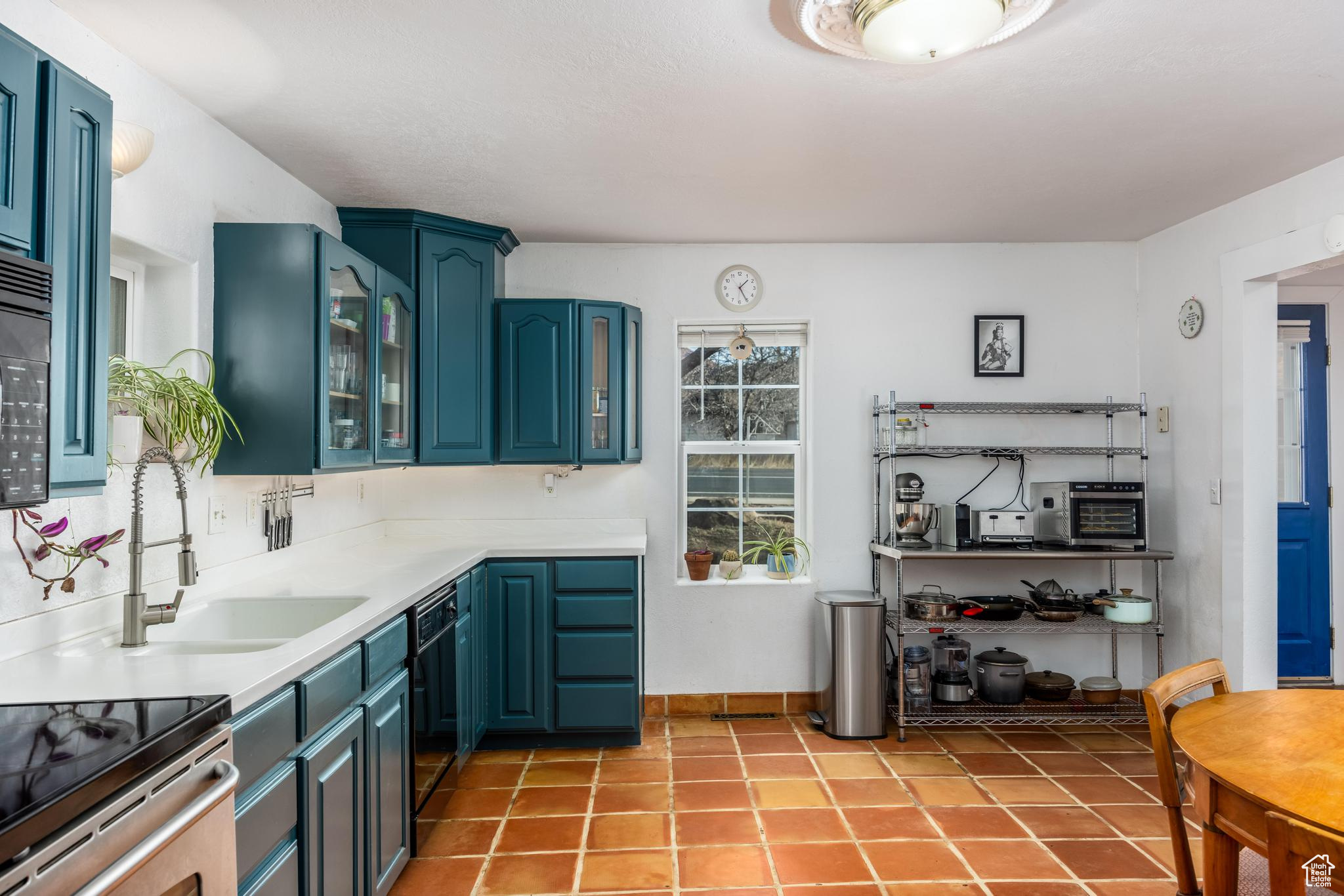 Kitchen featuring blue cabinetry, light tile patterned flooring, a sink, black appliances, and glass insert cabinets