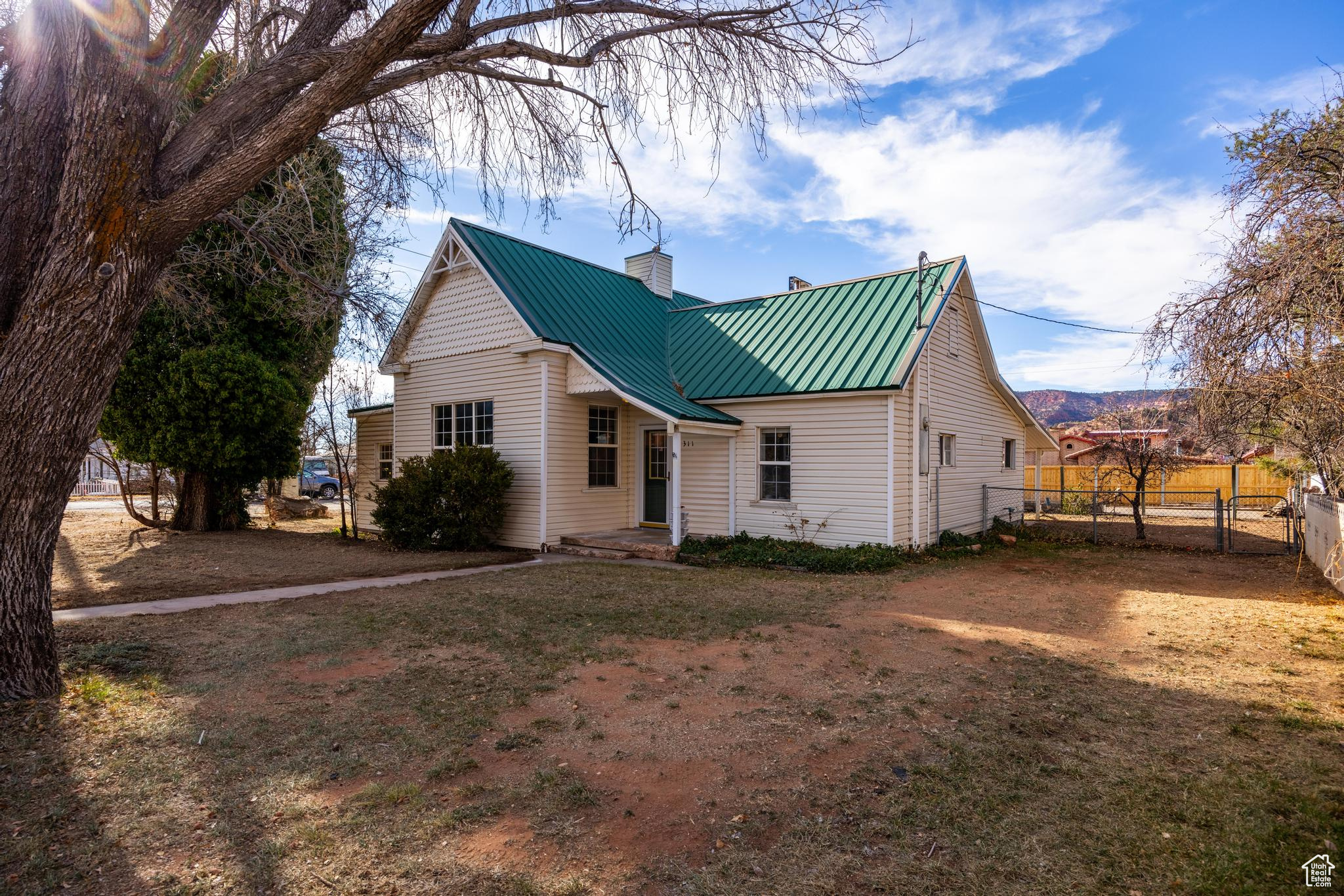 Back of house with a gate, fence, a standing seam roof, a chimney, and metal roof