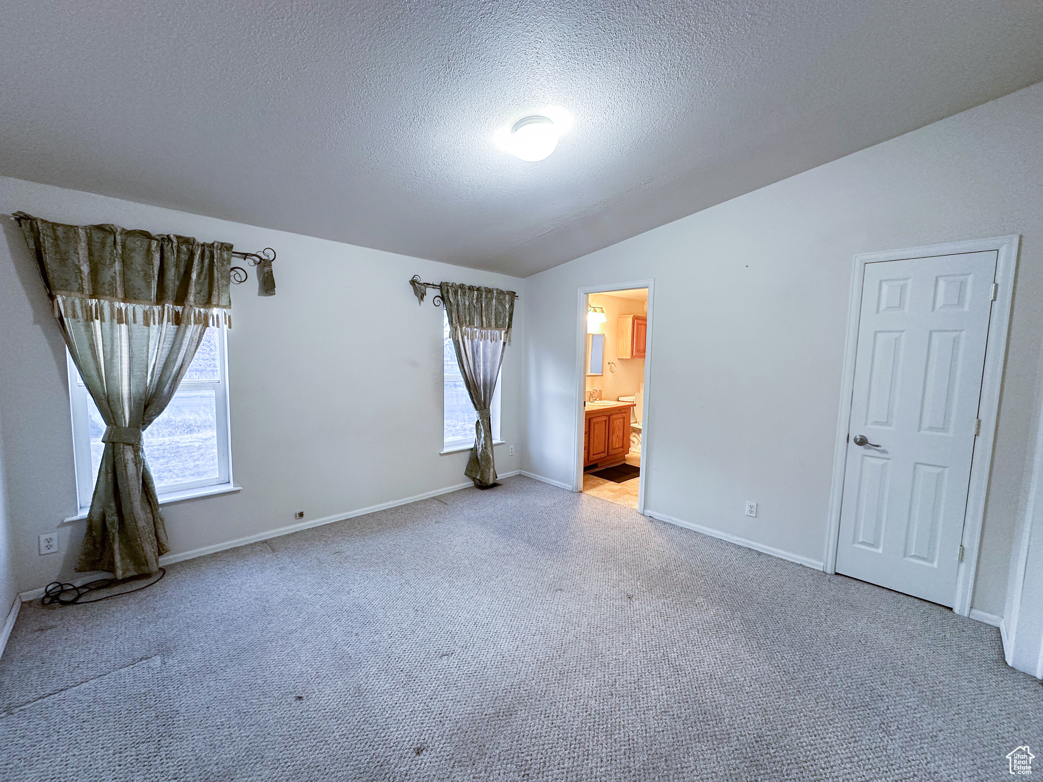 Unfurnished bedroom with lofted ceiling, ensuite bath, a textured ceiling, carpet flooring, and multiple windows