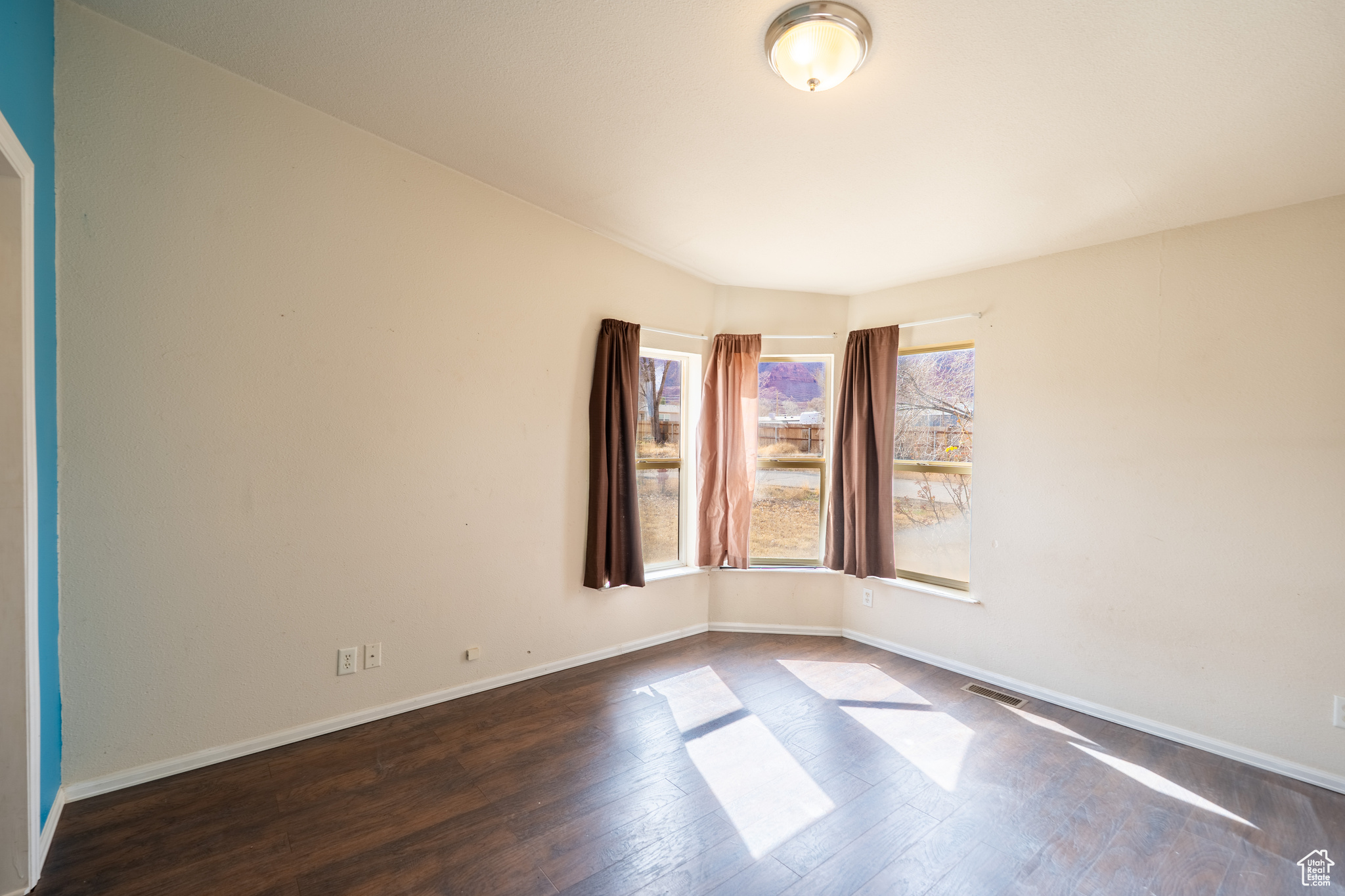 Empty room featuring dark wood-style flooring, visible vents, and baseboards