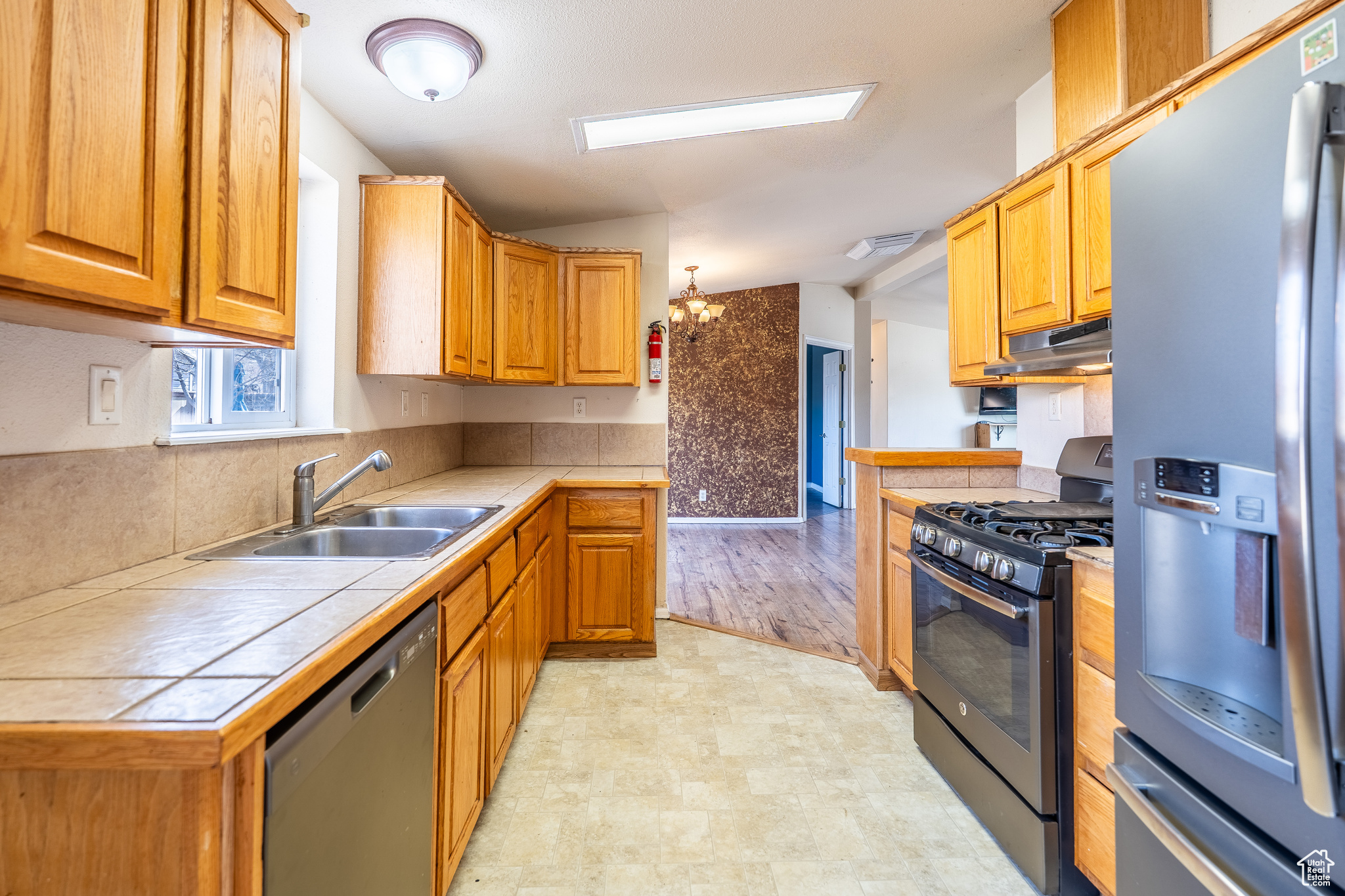 Kitchen featuring tile countertops, under cabinet range hood, stainless steel appliances, a sink, and light floors