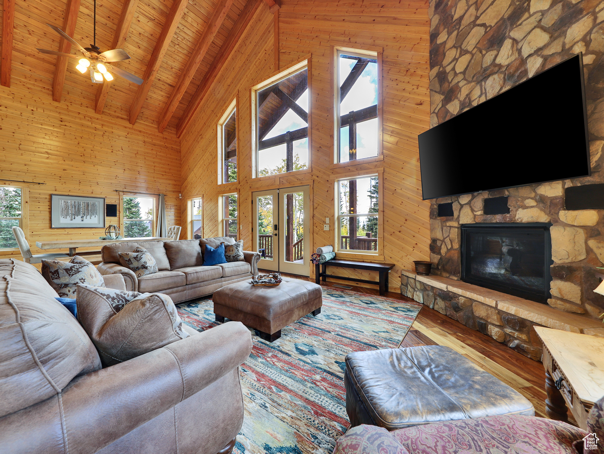 Living room featuring wood walls, hardwood / wood-style floors, a stone fireplace, wooden ceiling, and plenty of natural light