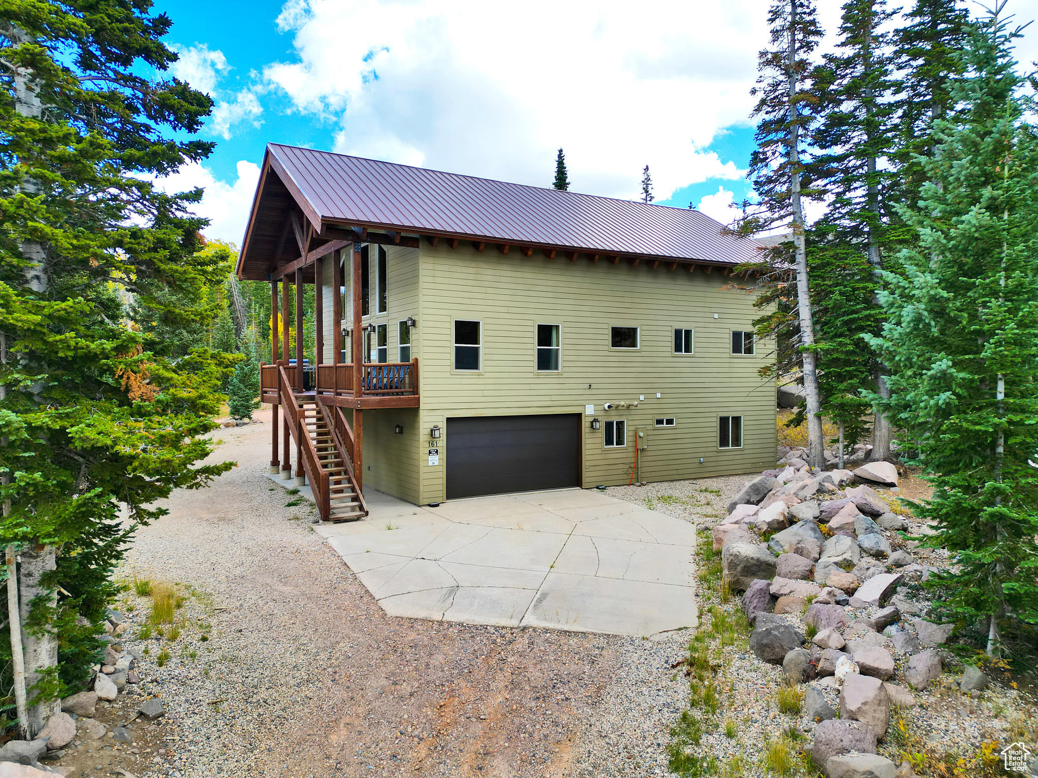 View of side of home featuring a deck, stairway, metal roof, concrete driveway, and a garage