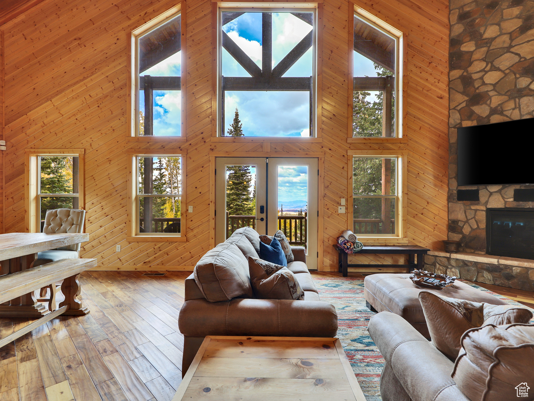 Living area featuring a stone fireplace, a high ceiling, wooden walls, and hardwood / wood-style floors