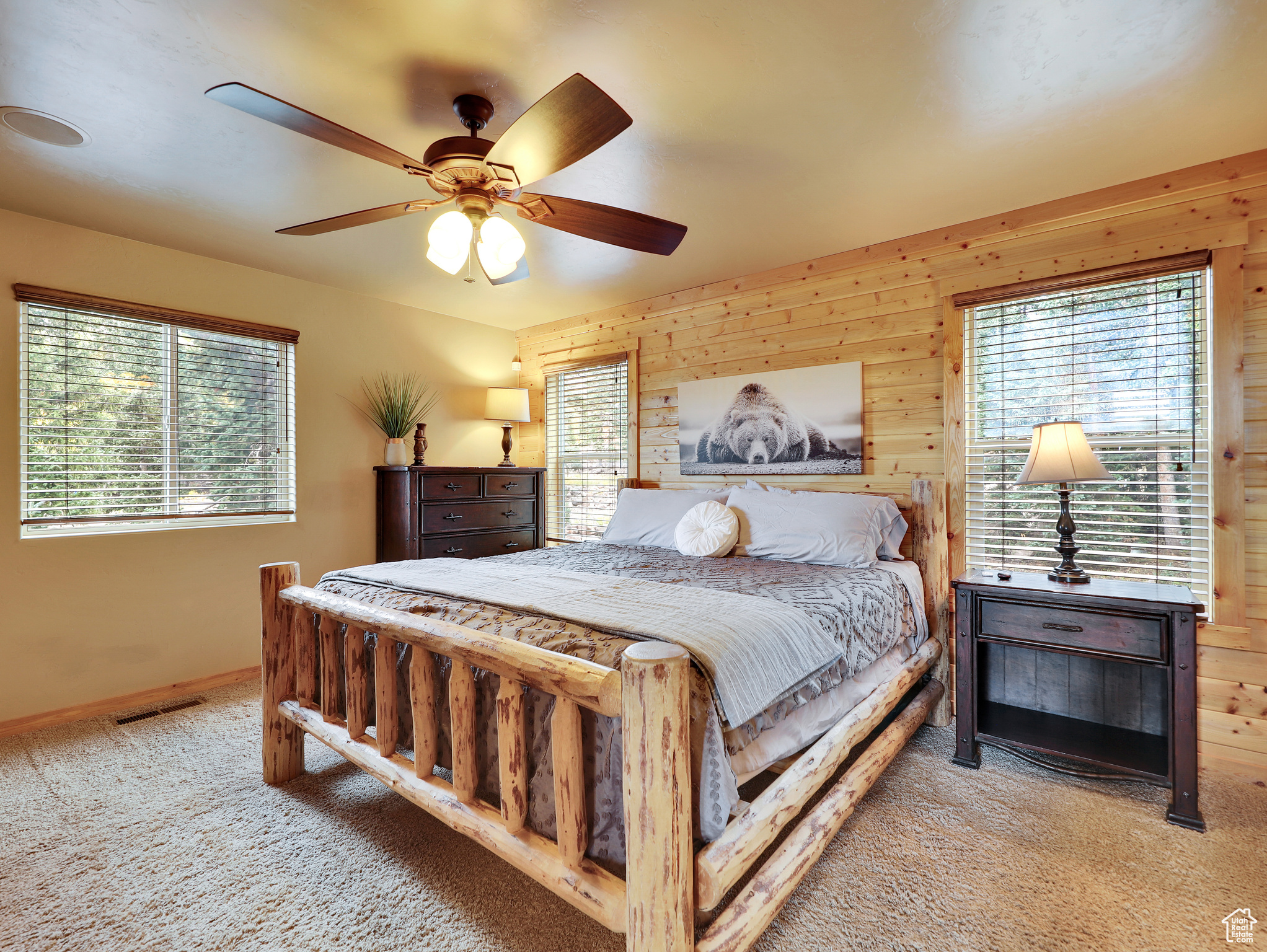 Carpeted bedroom with visible vents, multiple windows, and wood walls