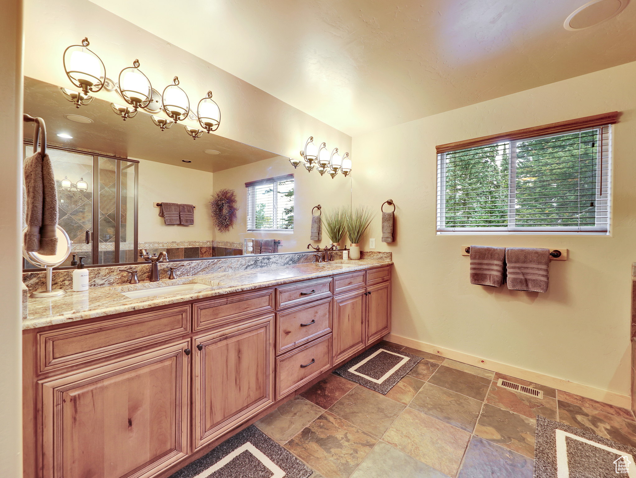 Full bath with double vanity, baseboards, visible vents, and a sink