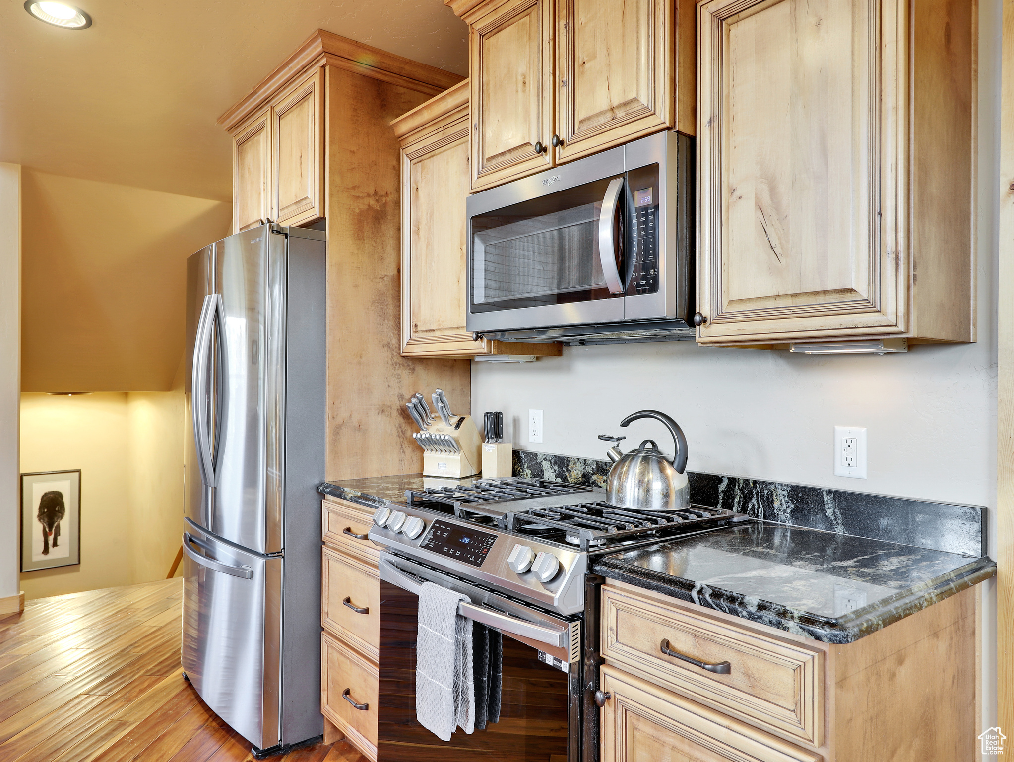 Kitchen featuring dark stone countertops, stainless steel appliances, and light brown cabinets
