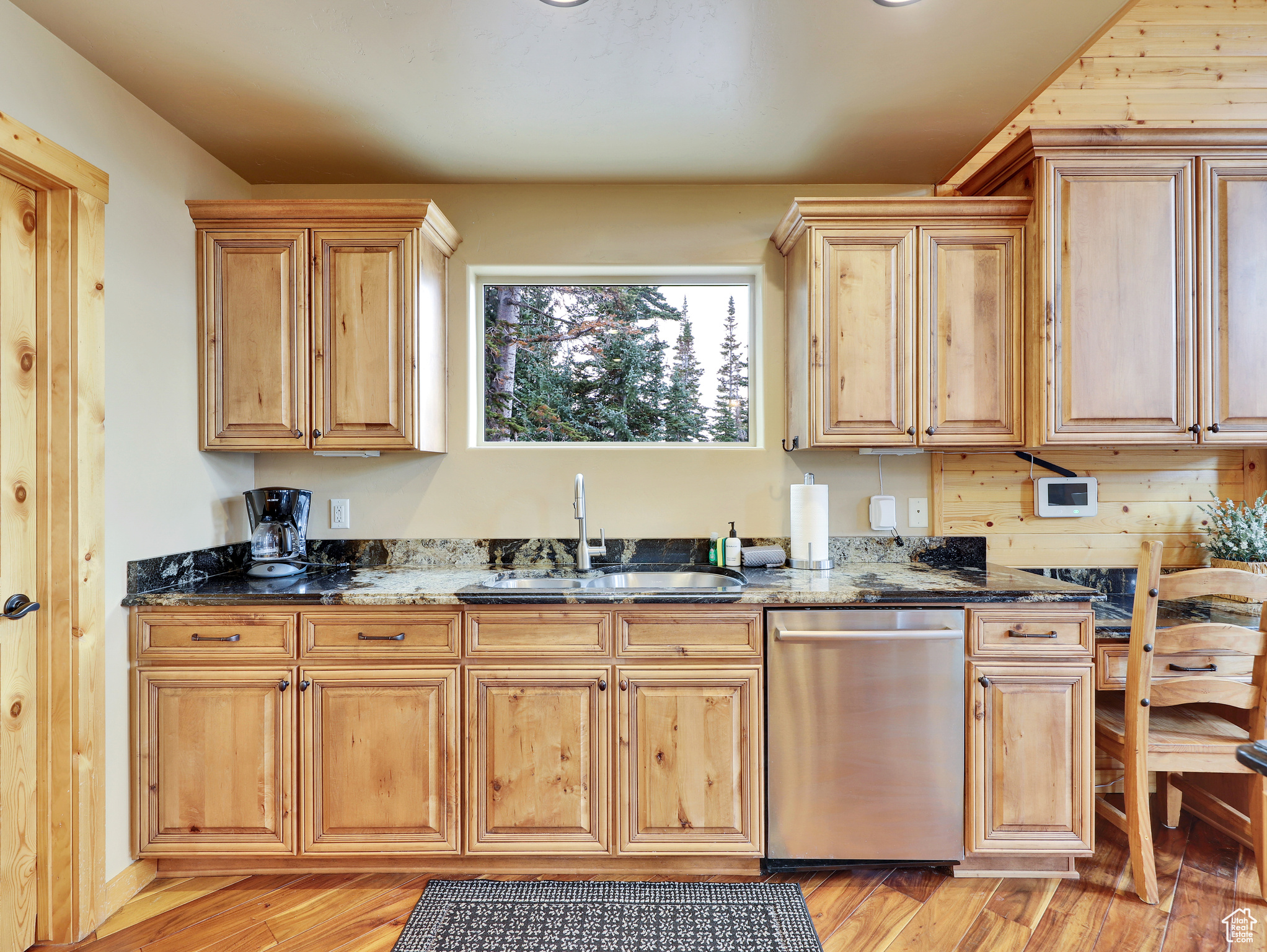 Kitchen featuring light brown cabinetry, dark stone counters, light wood-style flooring, stainless steel dishwasher, and a sink