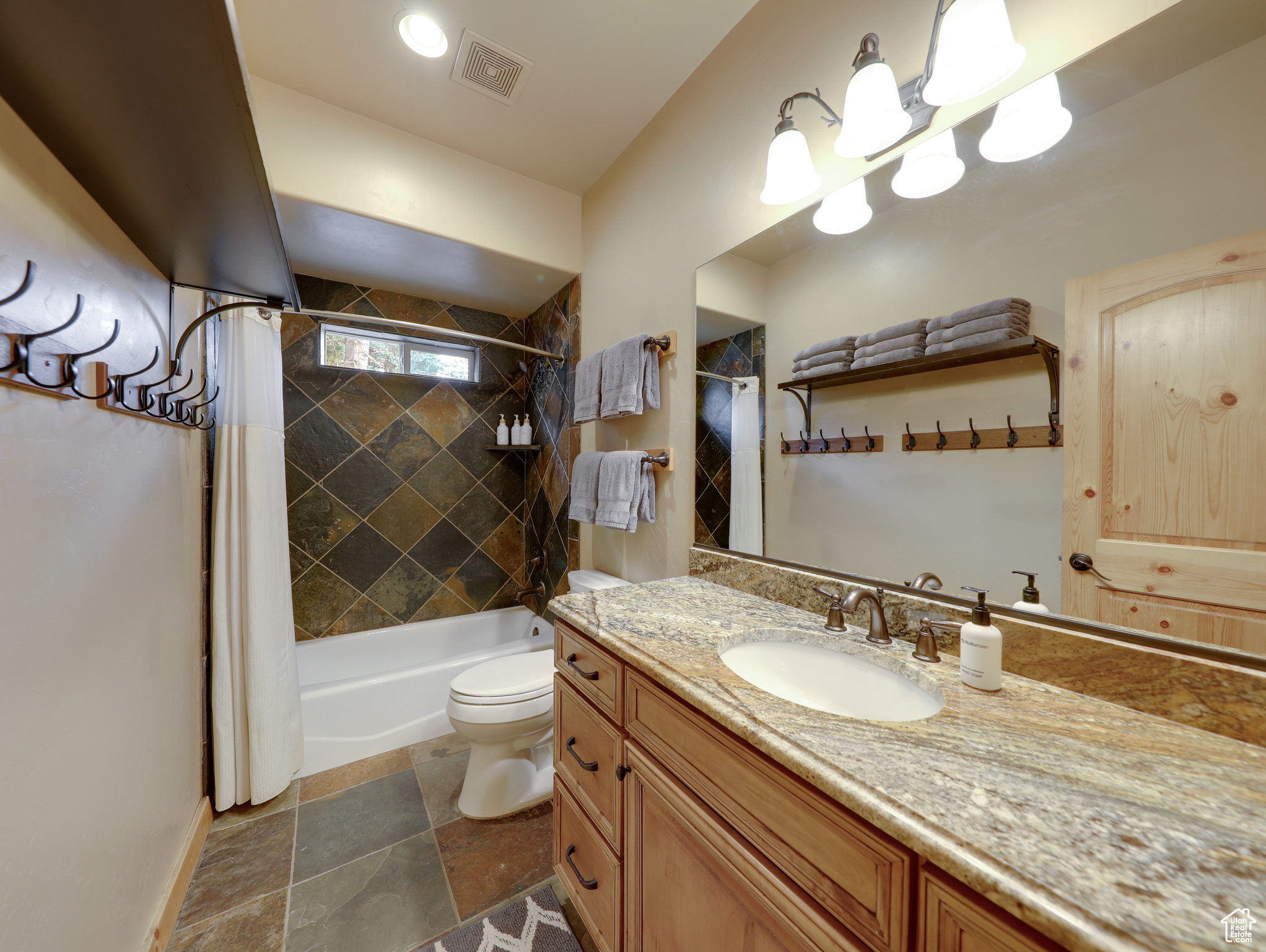 Full bath with vanity, visible vents, shower / bath combo, stone tile flooring, and toilet