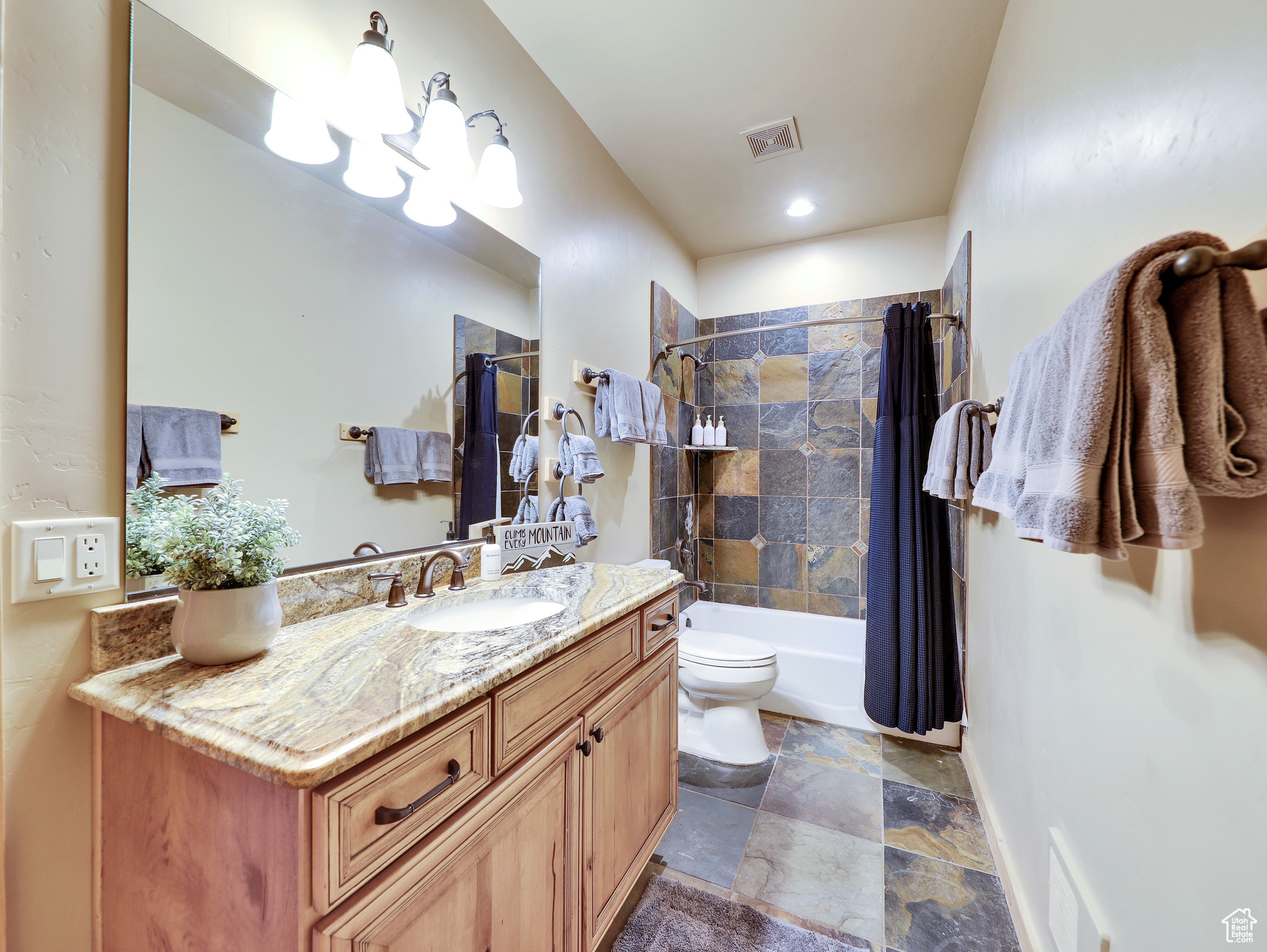 Bathroom featuring vanity, shower / bathtub combination with curtain, visible vents, and stone tile flooring