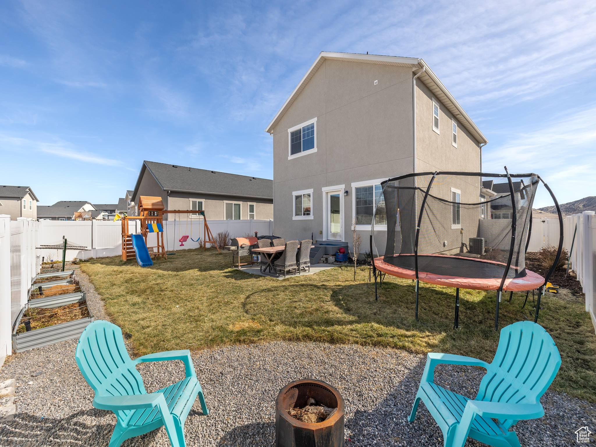 Back of property with a fire pit, a playground, a trampoline, stucco siding, and a fenced backyard