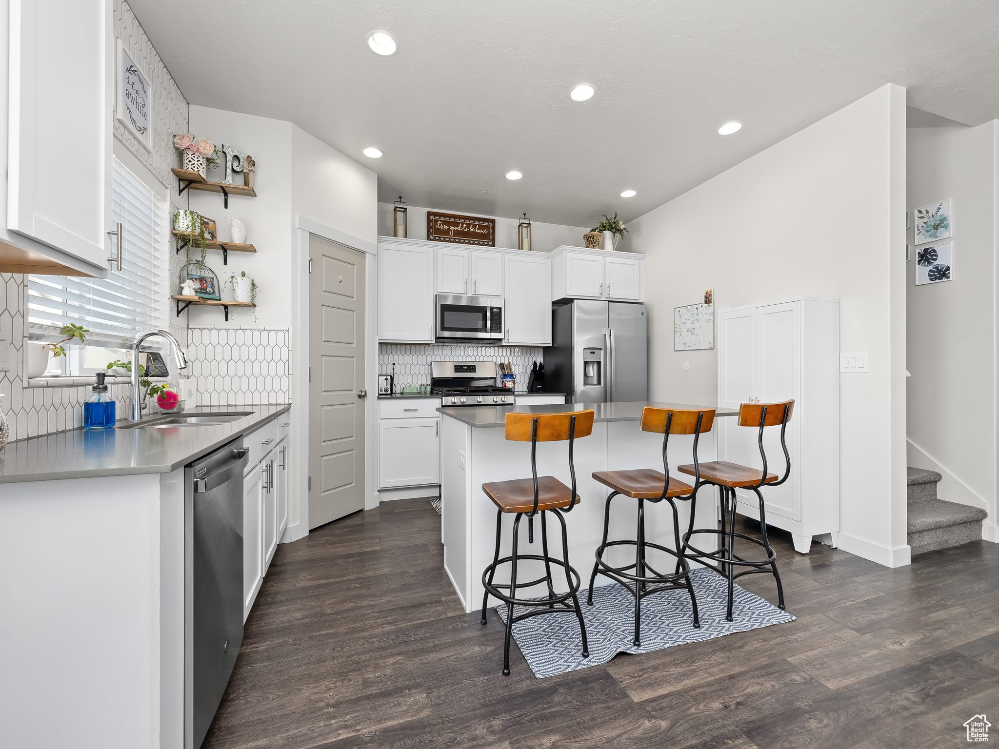 Kitchen featuring a kitchen island, a kitchen bar, appliances with stainless steel finishes, white cabinets, and a sink
