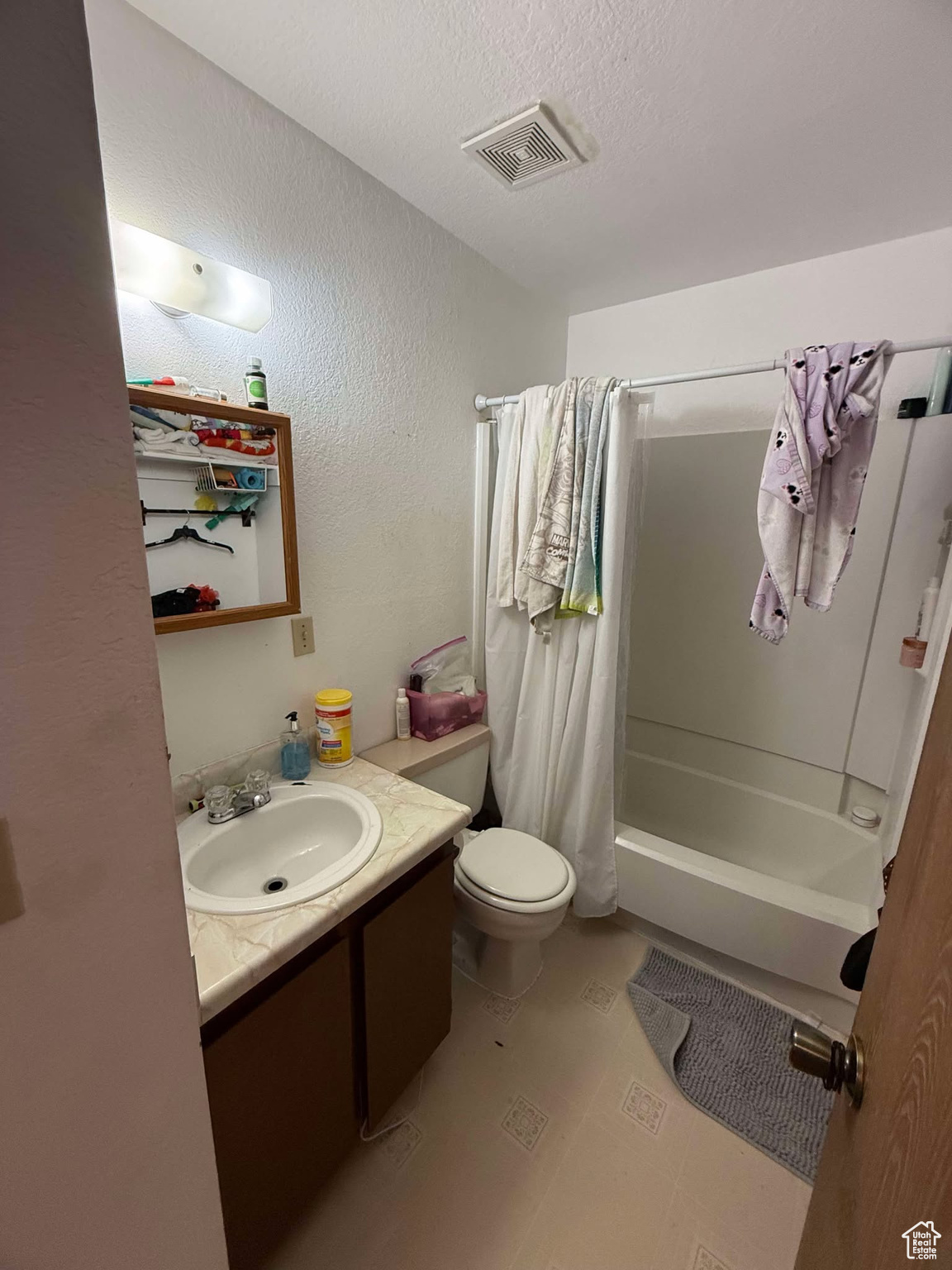 Full bath with vanity, visible vents, shower / bath combo with shower curtain, a textured ceiling, and toilet