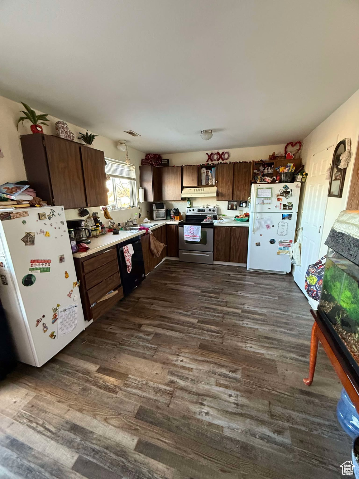 Kitchen with freestanding refrigerator, dark wood-style floors, electric stove, and black dishwasher
