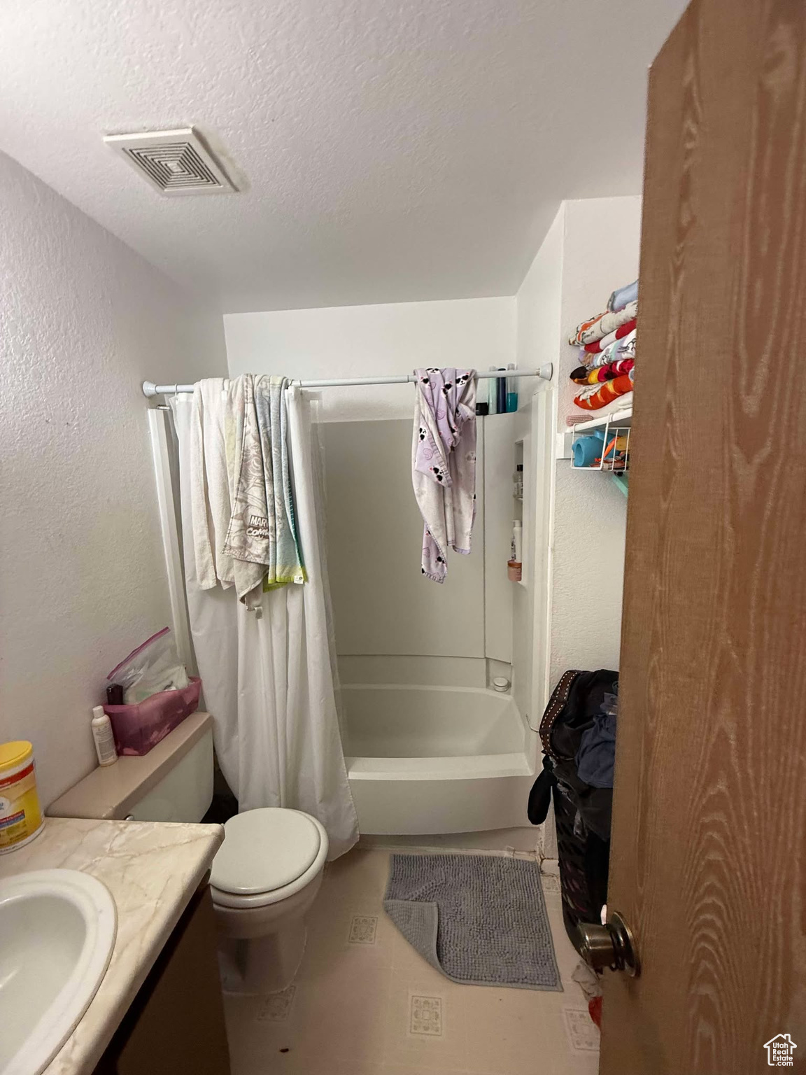Bathroom with visible vents, vanity, a textured wall, shower / bath combination with curtain, and a textured ceiling