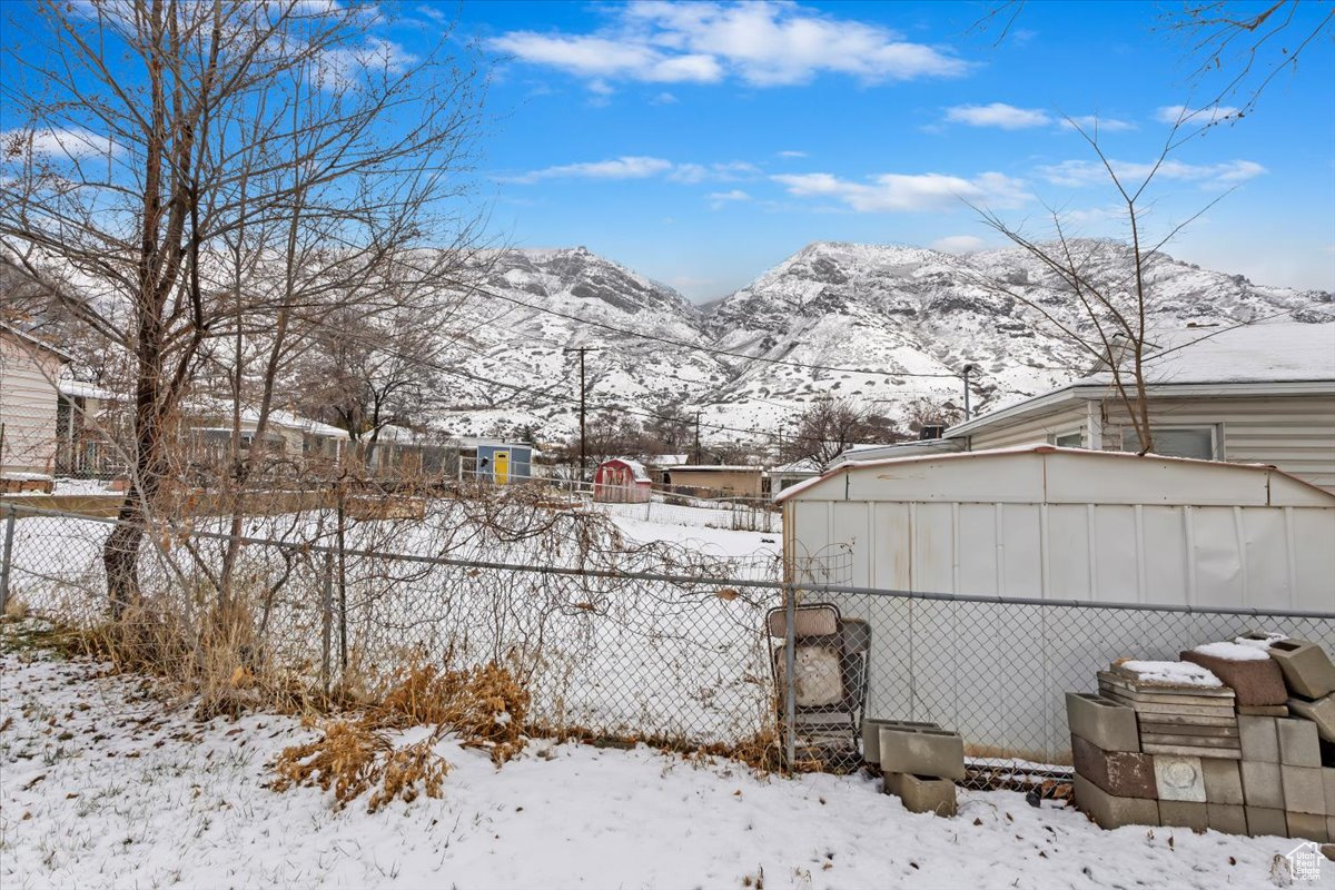 Yard covered in snow featuring a mountain view and fence
