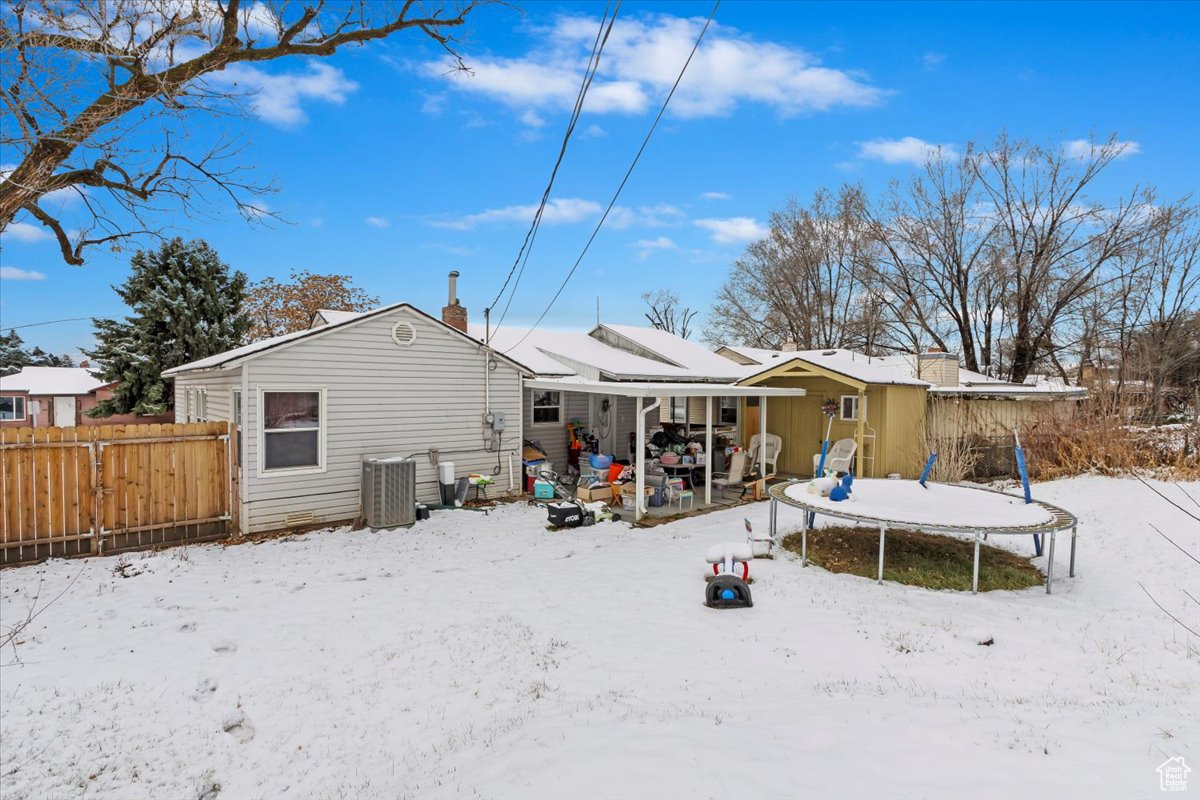Snow covered rear of property with a chimney, a trampoline, and fence