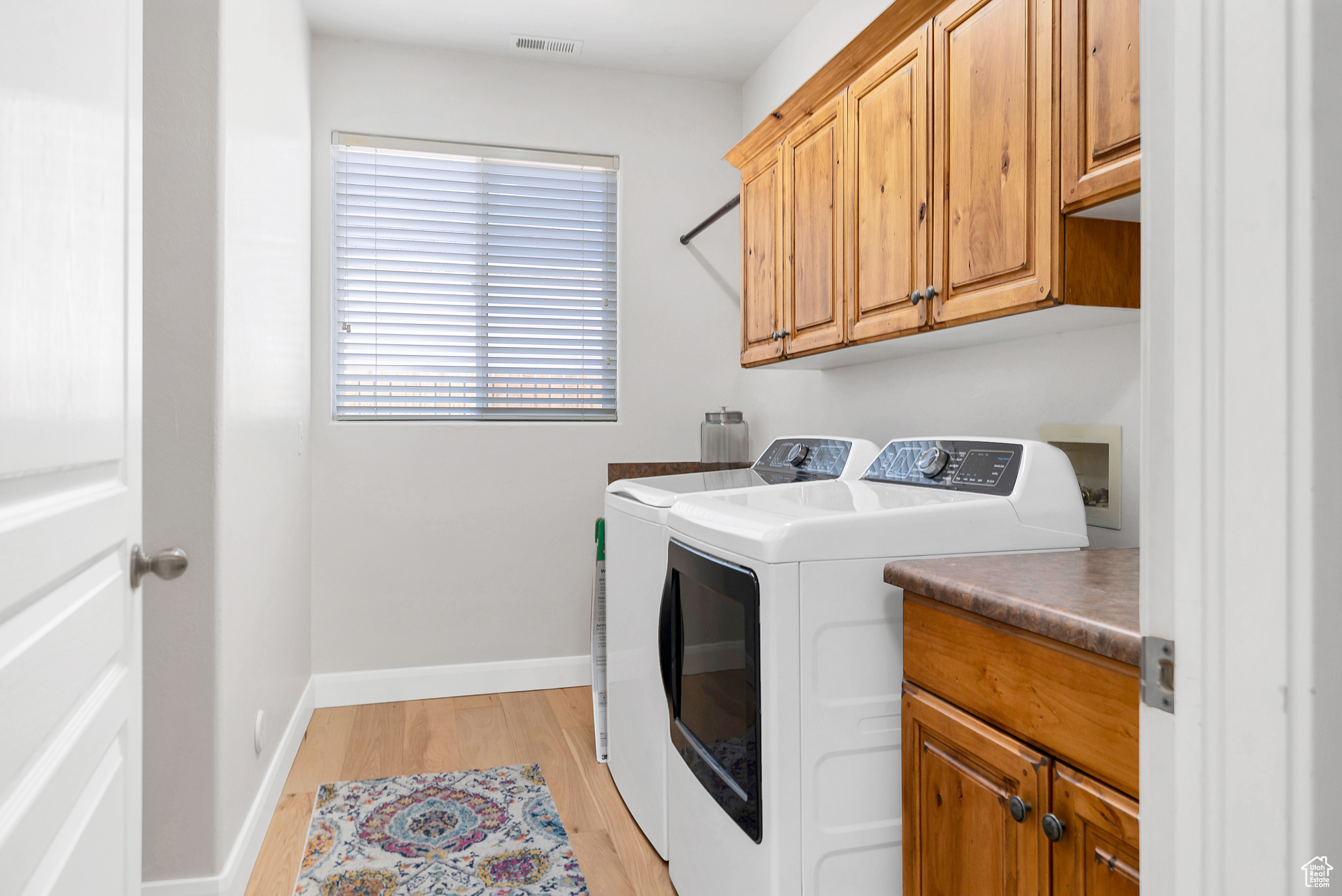 Laundry area with visible vents, baseboards, washer and clothes dryer, light wood-type flooring, and cabinet space